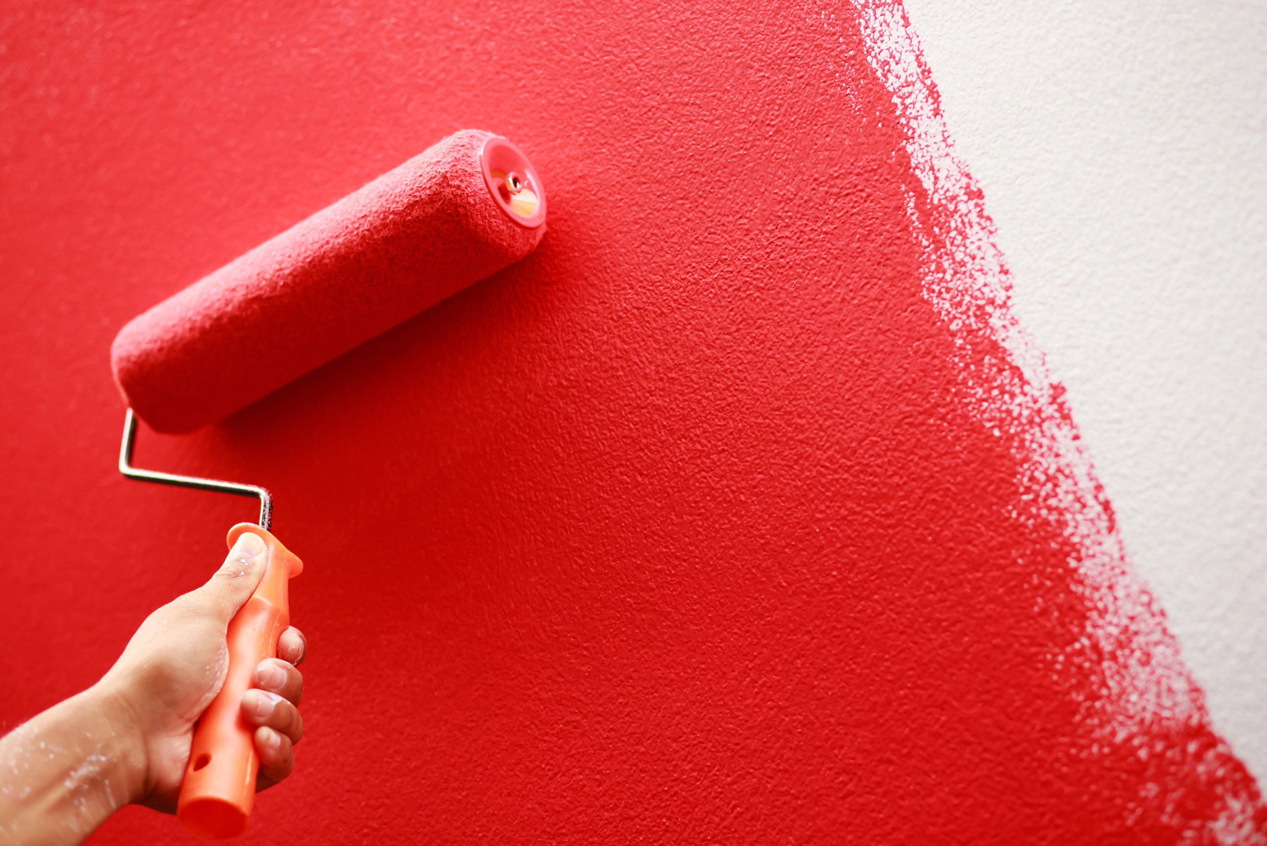Painting a wall red with paint roller.
