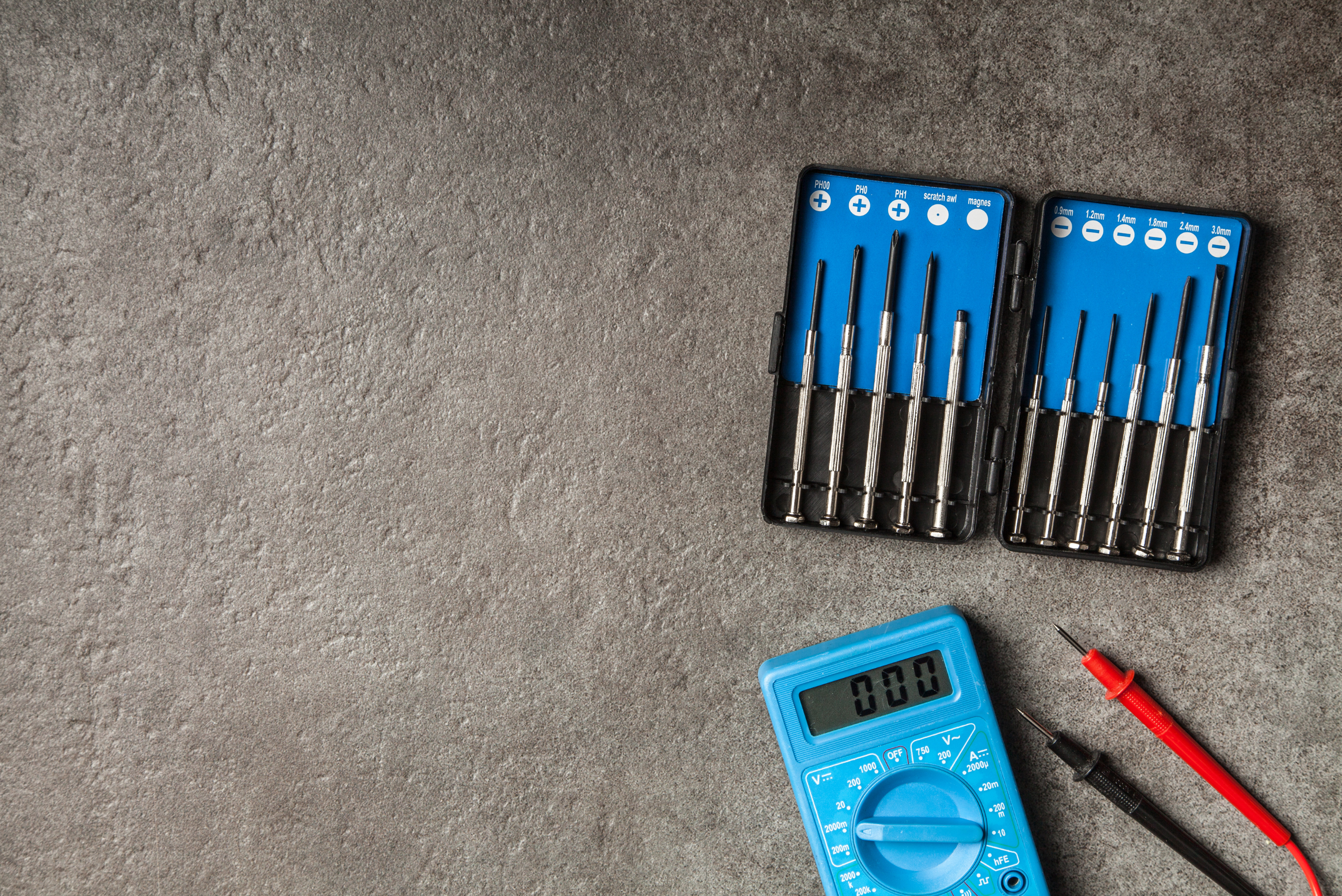A blue multimeter voltage tester and precision screw drivers.