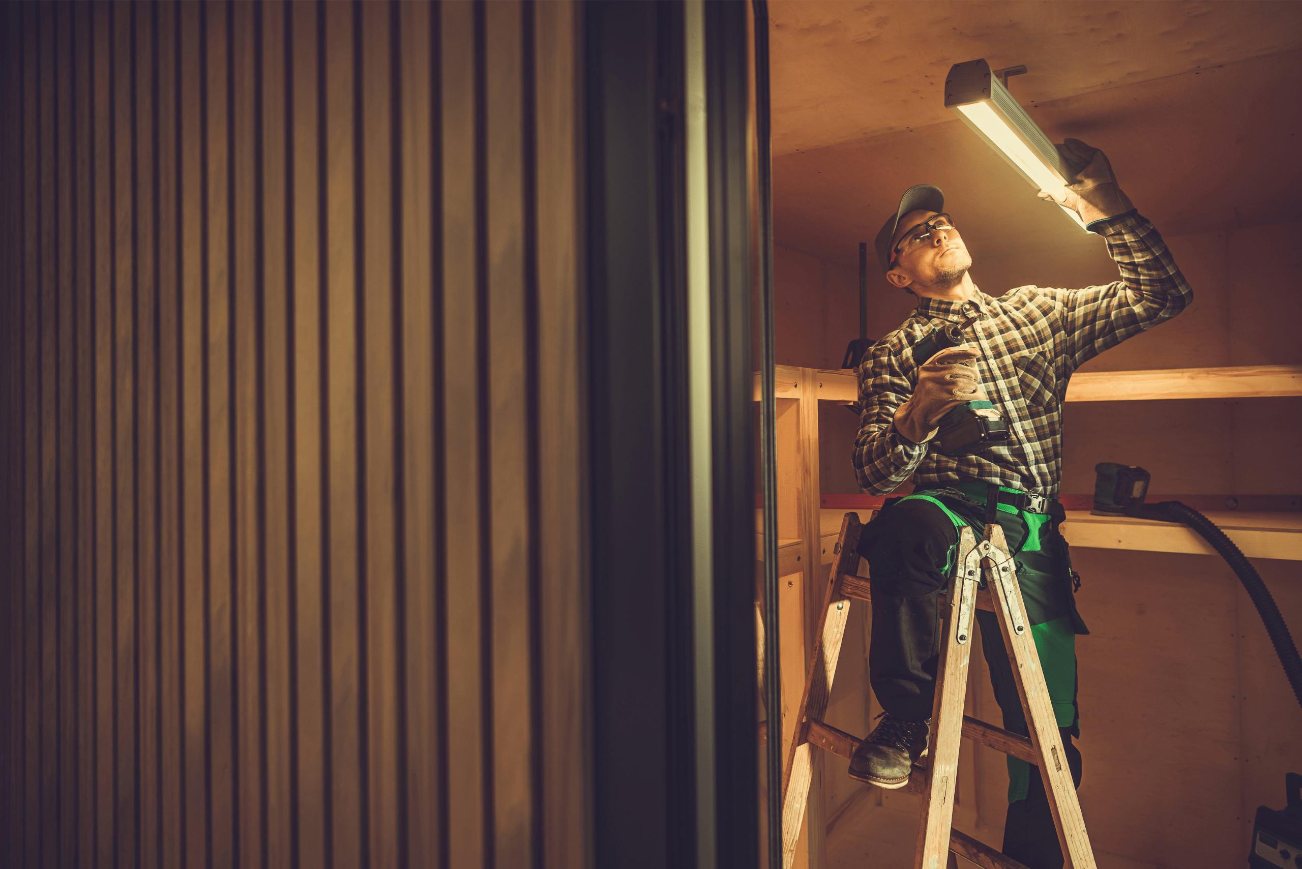 A man on ladder installs LED light fixtures.