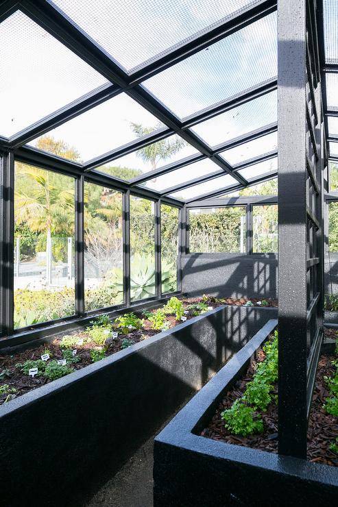 Positioned in a beautifully green backyard, a greenhouse is fitted with black planters.