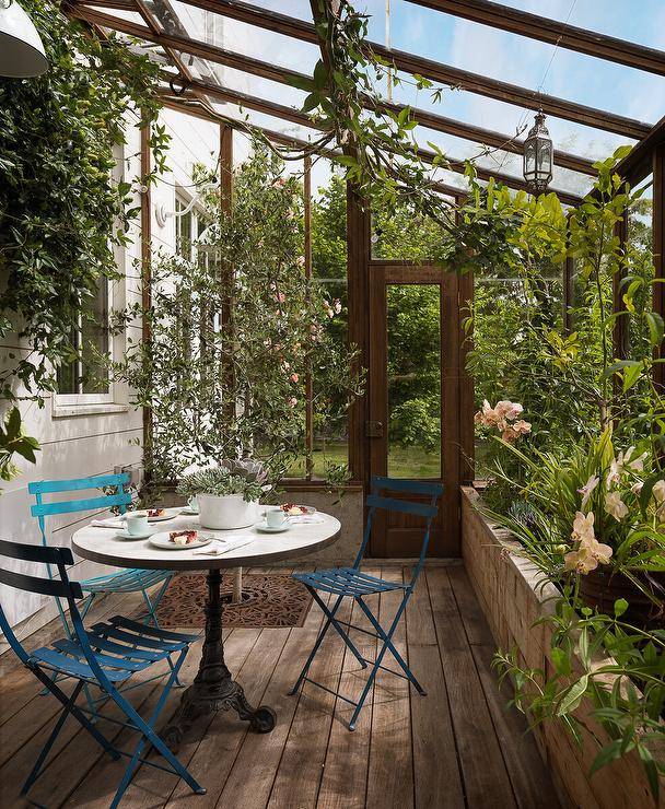 Cottage style greenhouse features blue metal chairs at a French bistro table.