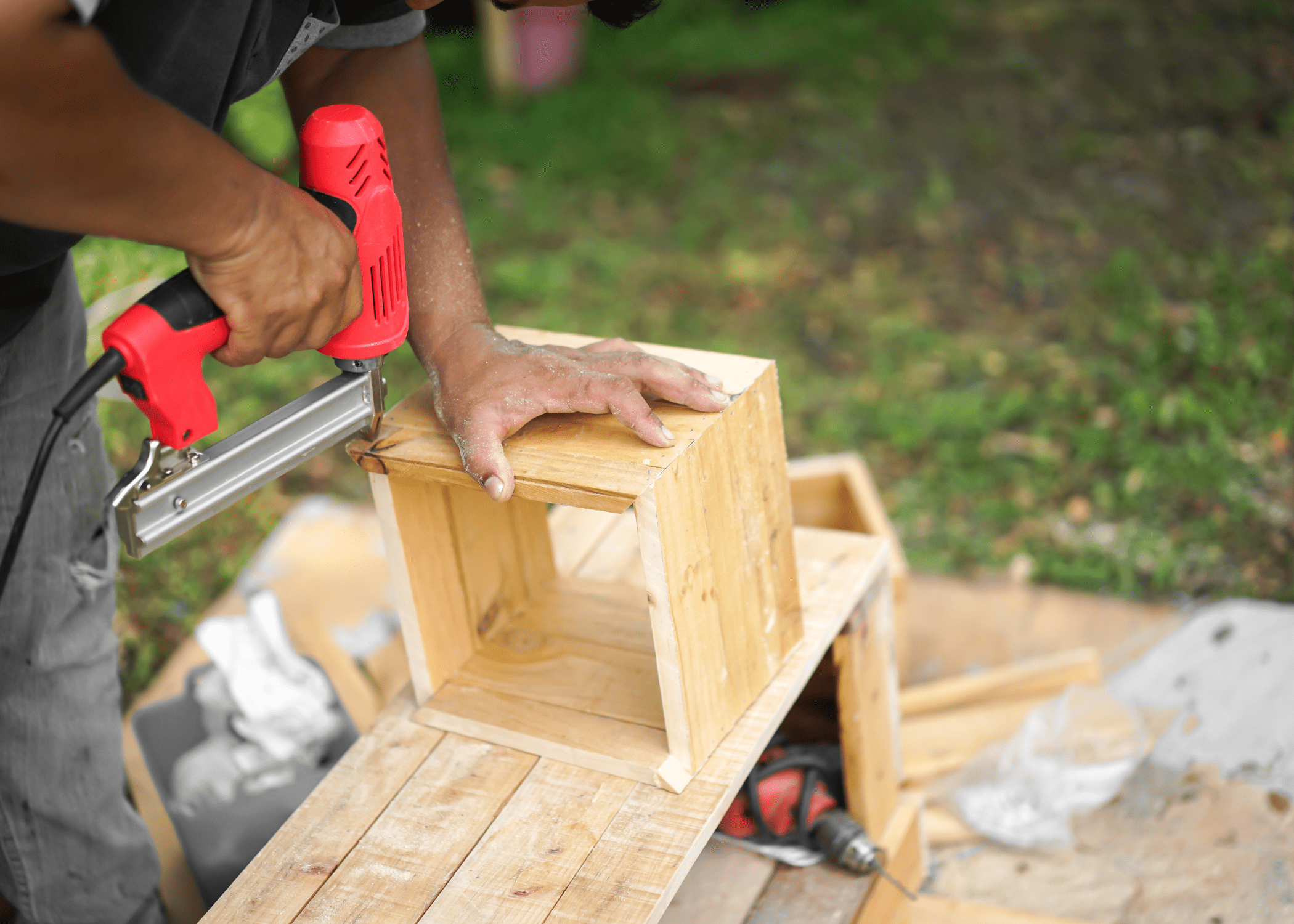 close up a red pin nailer and man using it to nail together a box frame