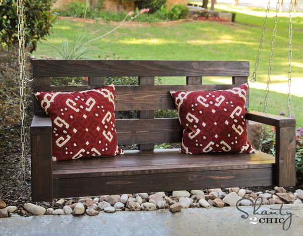 Dark brown wooden swing with throw pillows.