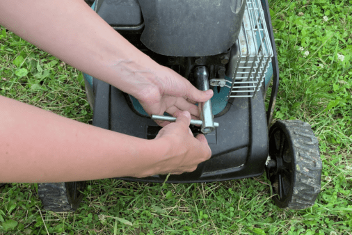 A closeup of someone's hands using a tool to remove spark plug from lawn mower engine.