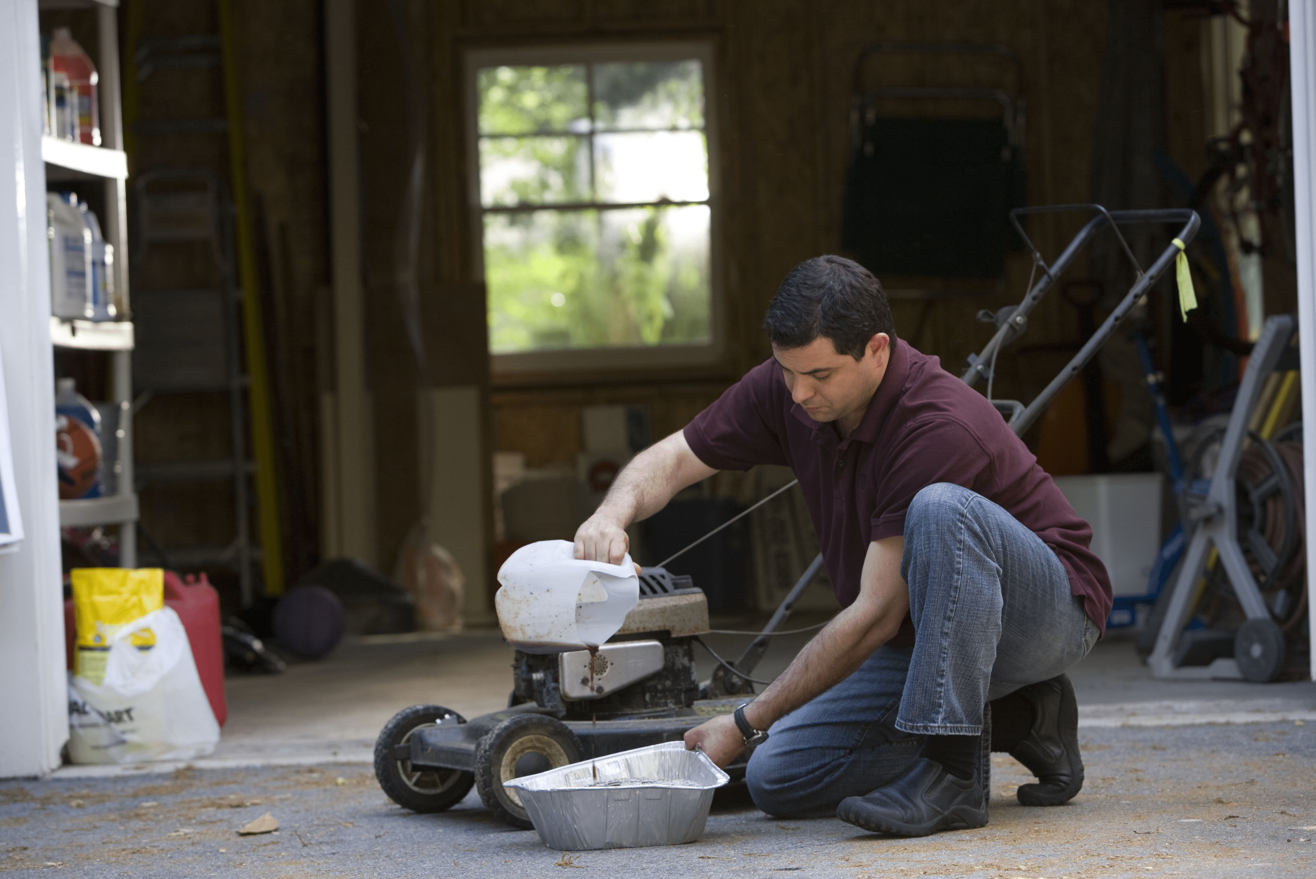 A man changing the oil on a lawn mower.