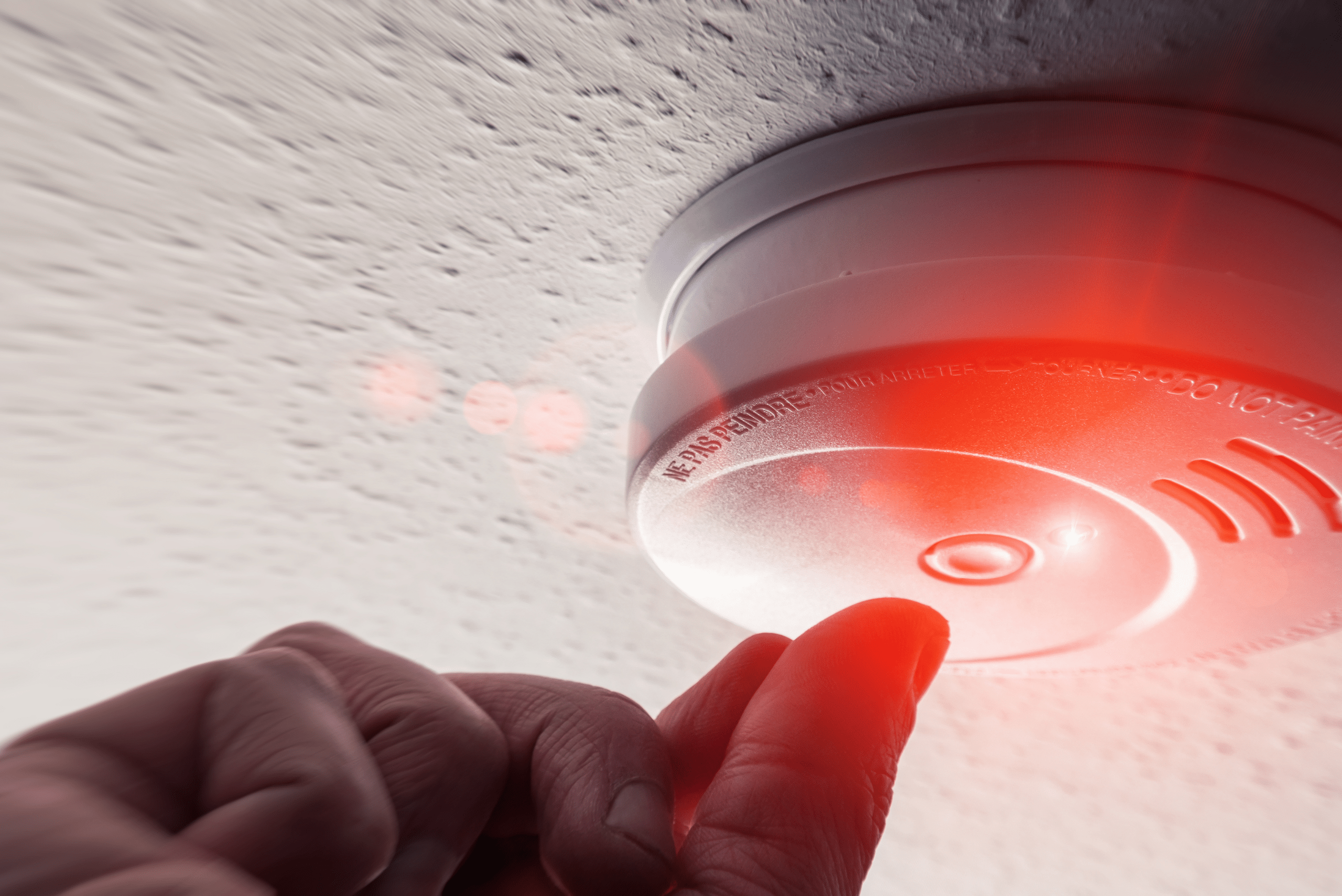 Hand pressing the button on a smoke alarm.