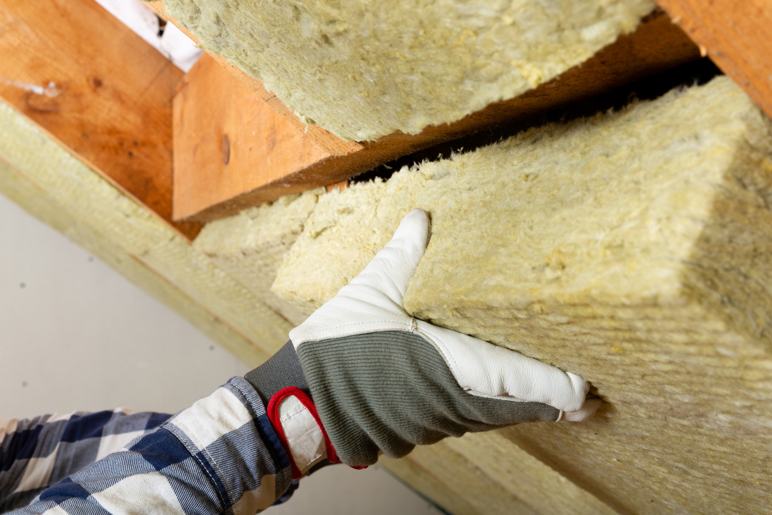 A worker's hand wearing gloves while installing insulation.