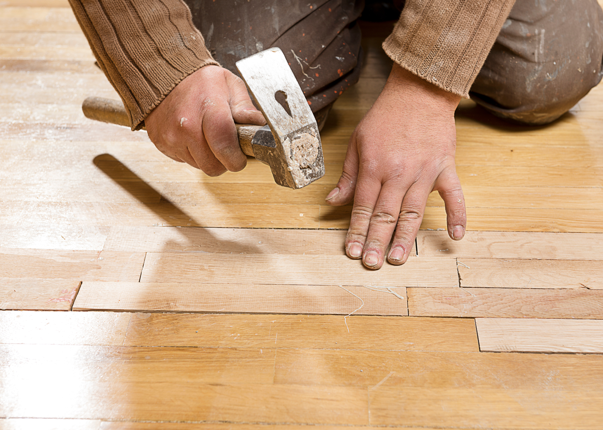 man hammering new pieces into hardwood floor