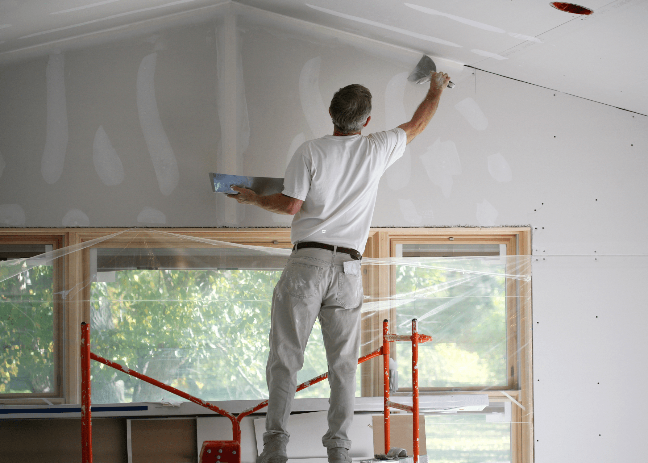 Man using spackle to finish drywall standing on scaffolding