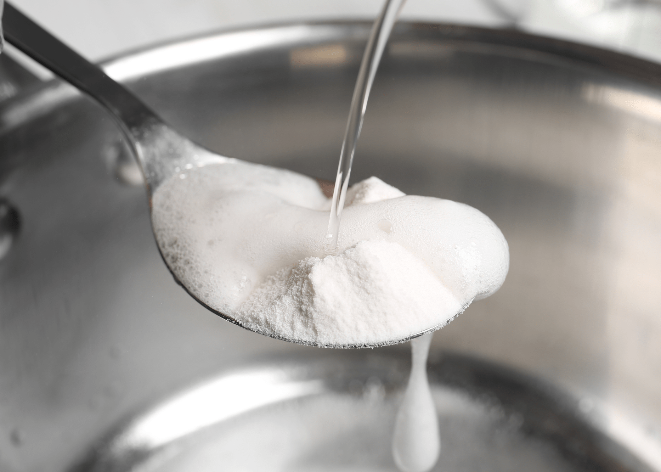 vinegar being poured onto a spoon with baking soda on it