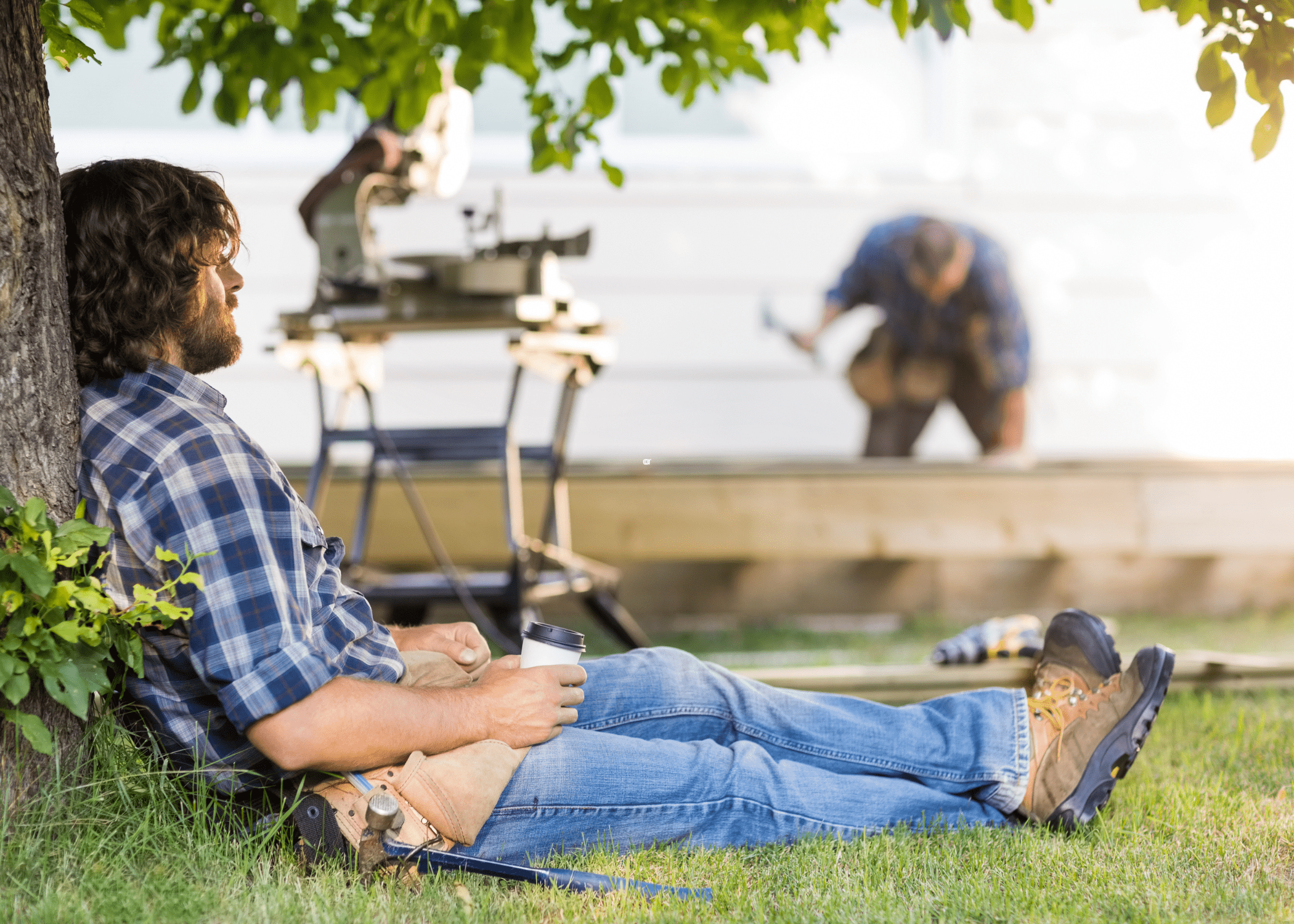 man taking a break on outdoor construction site with another blurred man working in the background