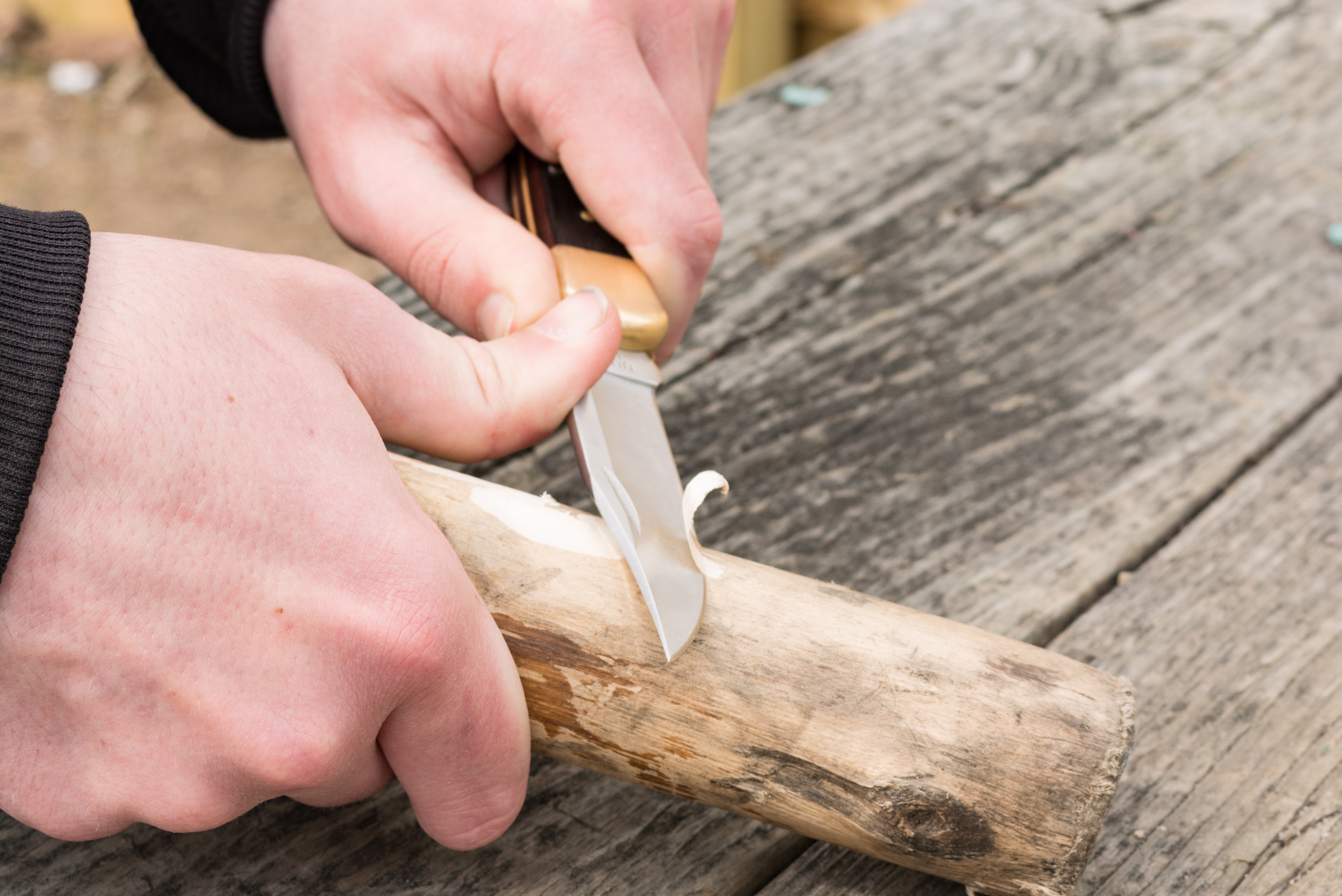 Hands whittling wooden stick.