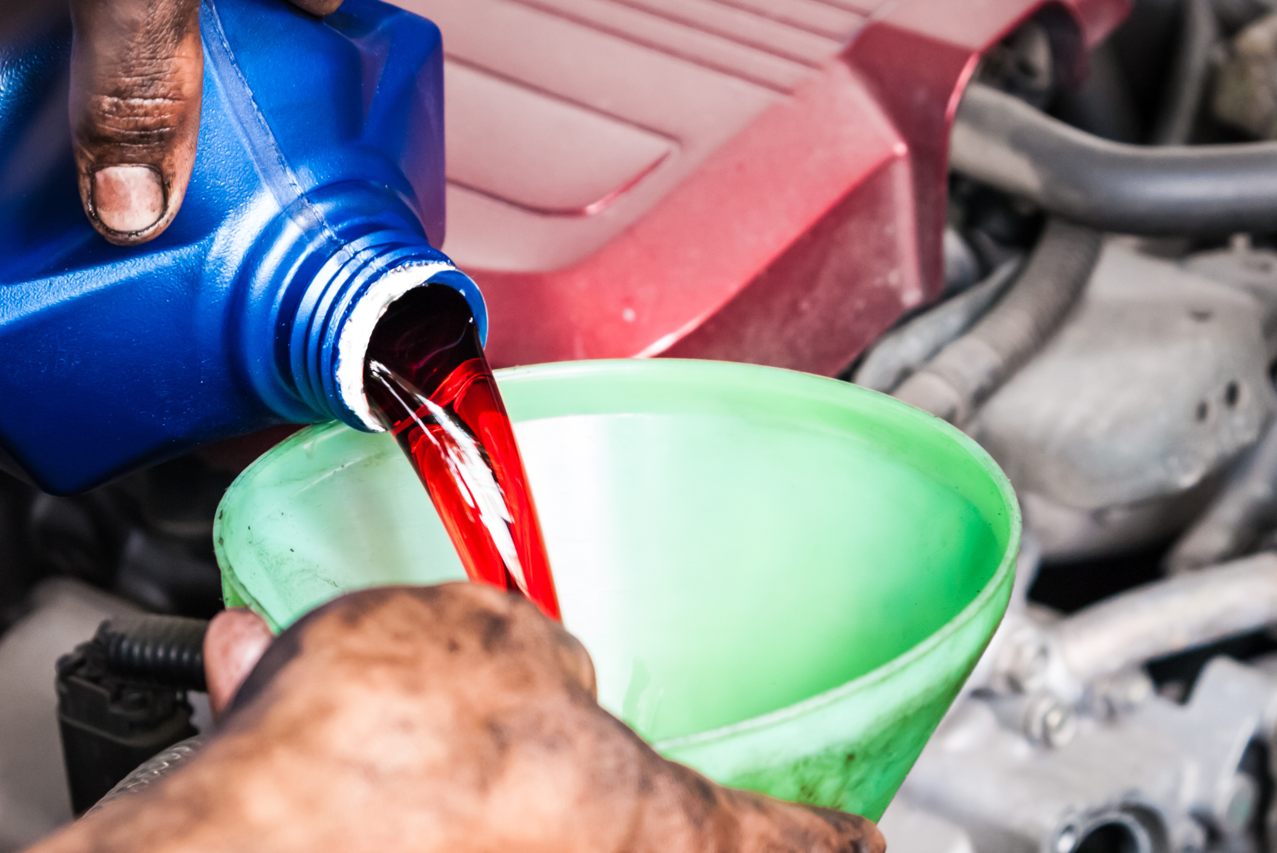 Bottle of transmission fluid pouring red oil into green funnel.