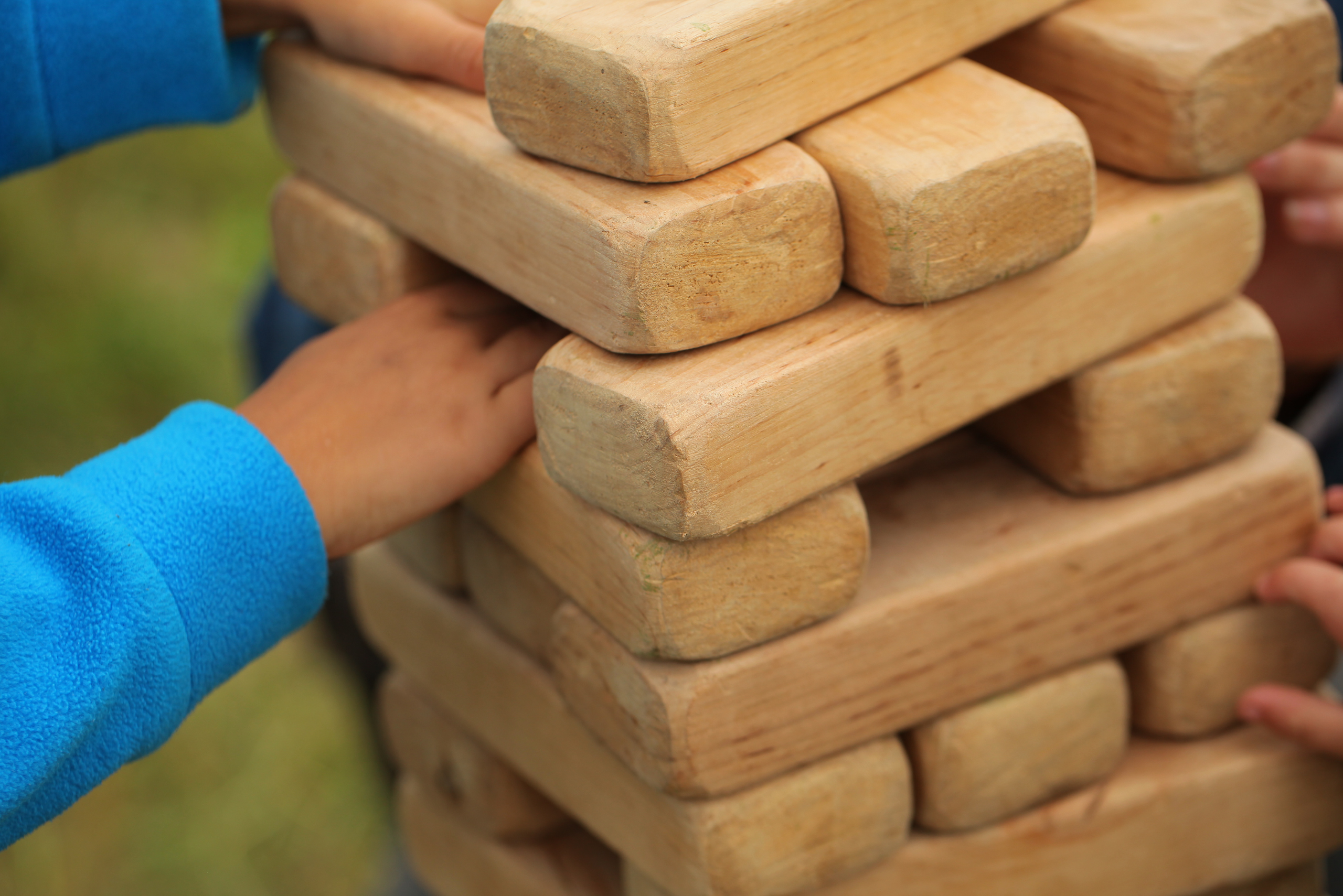 A boy wearing blue playing with giant Jenga game.