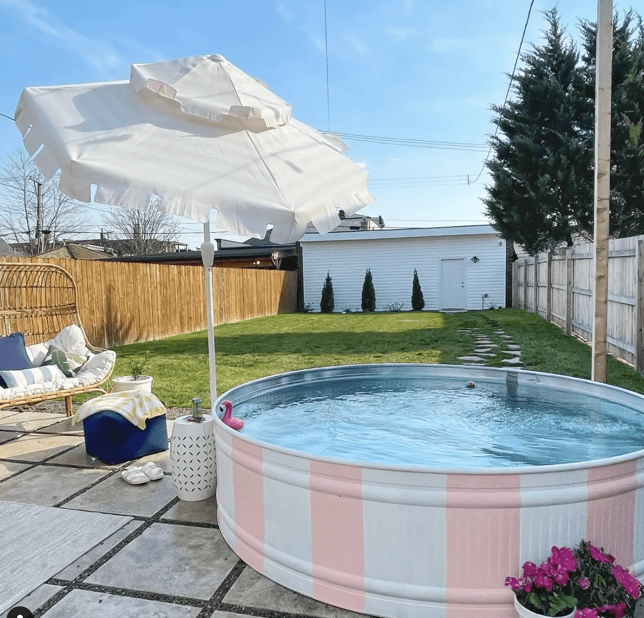 pink and white painted stock tank pool in backyard with white umbrella