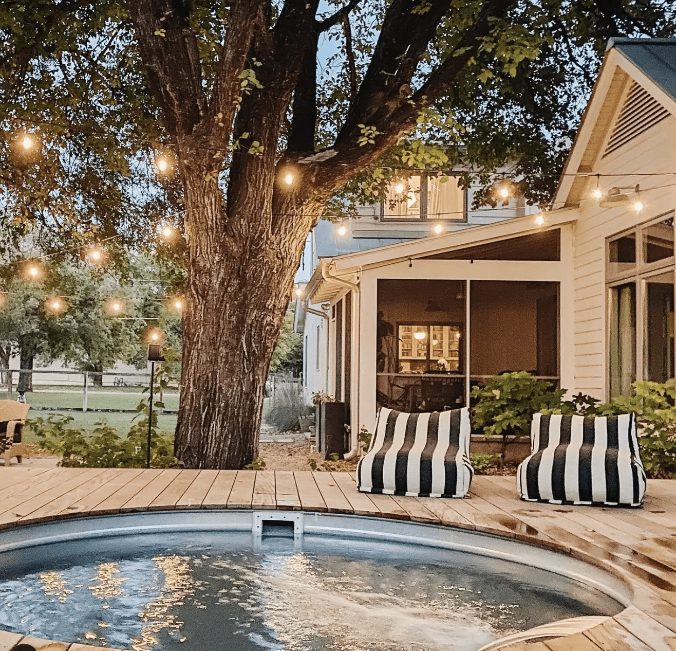 pretty backyard stock tank pool at night with built around deck and string lights