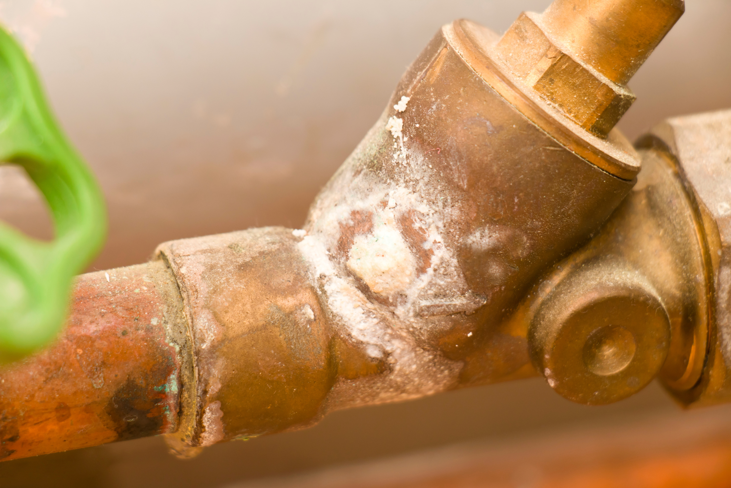 A rusty water shut-off valve pipe with green valve.