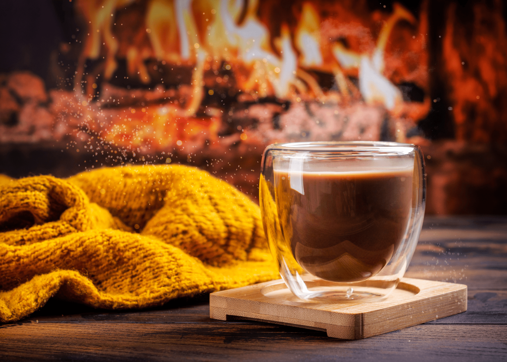 wood coaster with hot chocolate on it in clear glass with fire in background