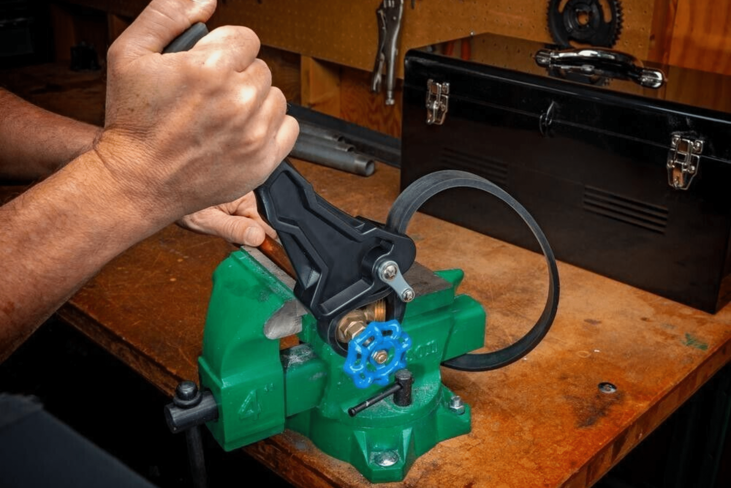 A strap wrench tightening a water valve in green vise.