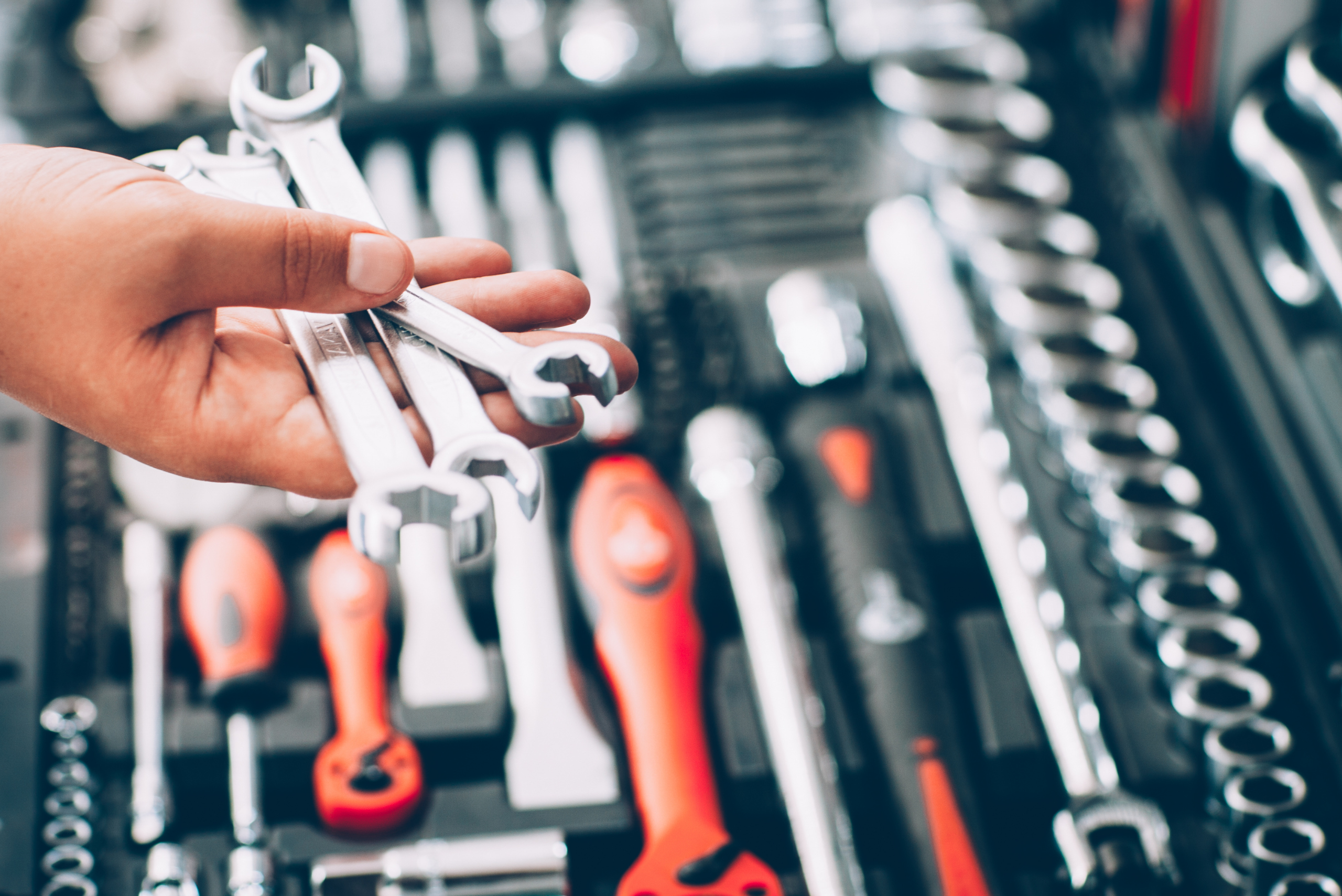 Hand holding wrenches above tool kit.