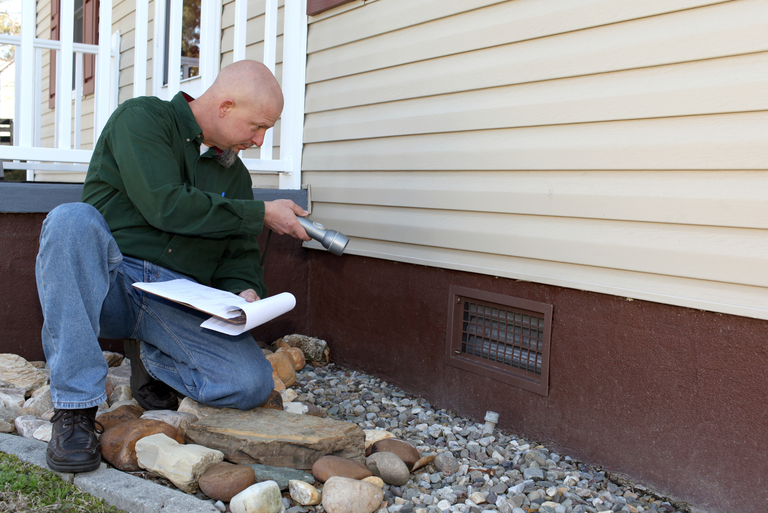 A man inspecting the foundation of a house.