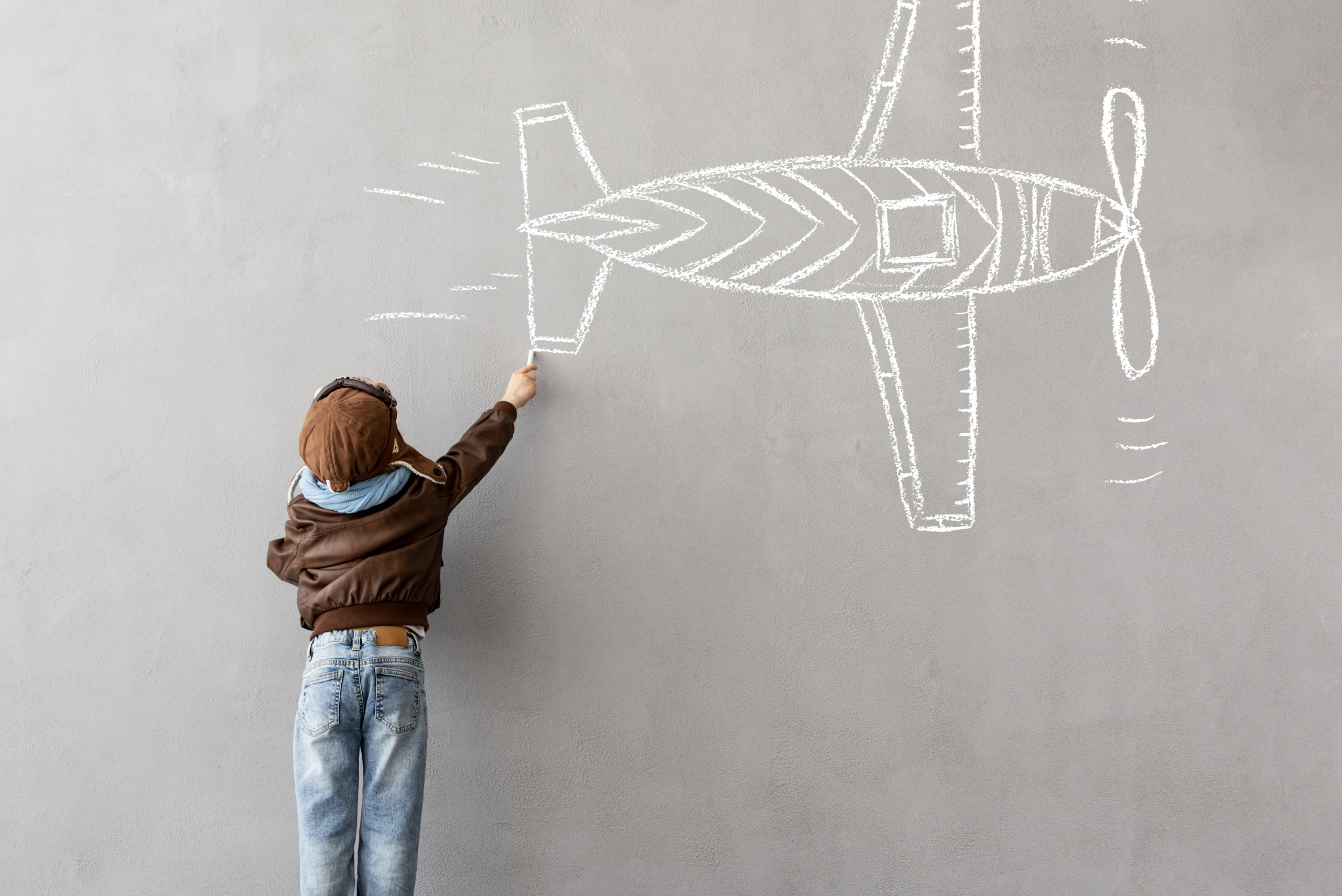 Kid drawing a plane on a chalk wall.