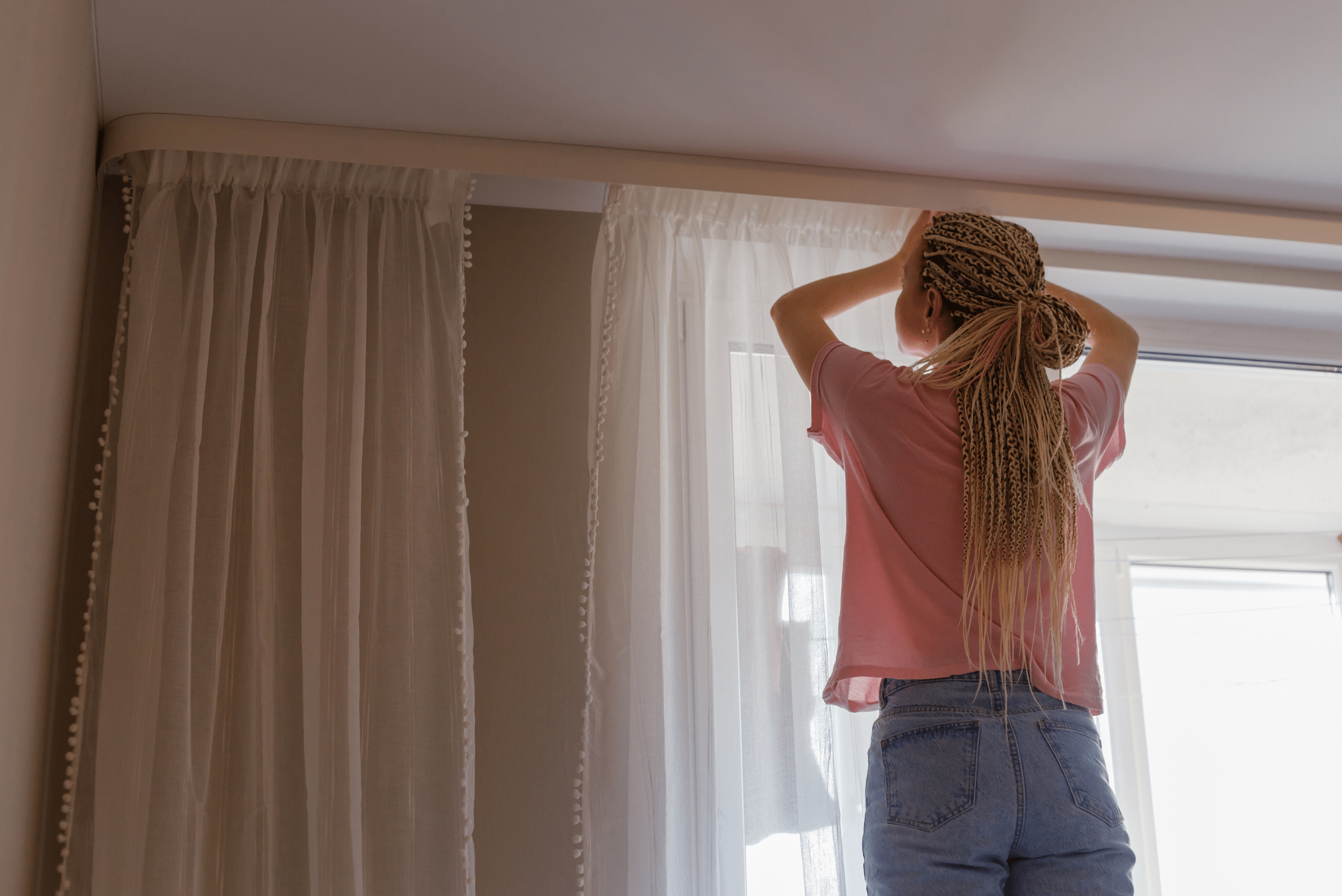 Woman hanging curtains in a living room.