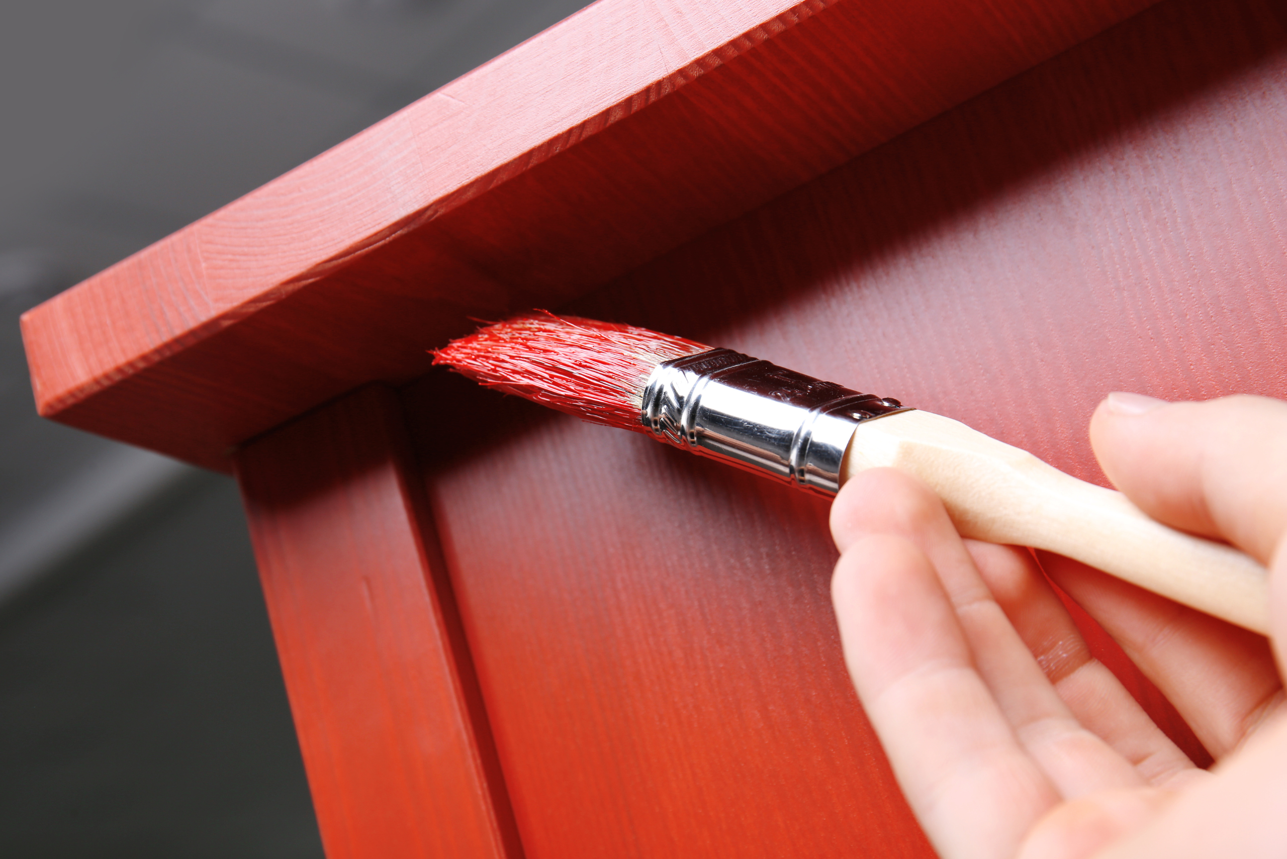 Repainting a piece of furniture red with brush.