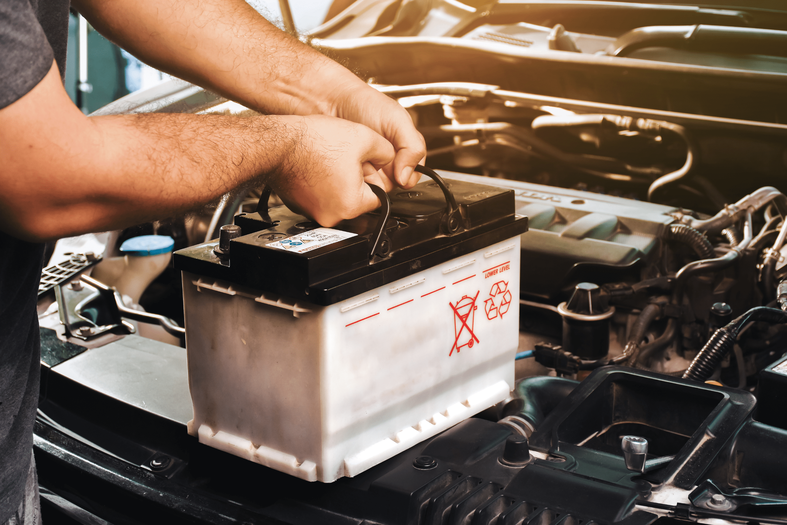 Person holding onto a car battery in front of an engine bay.