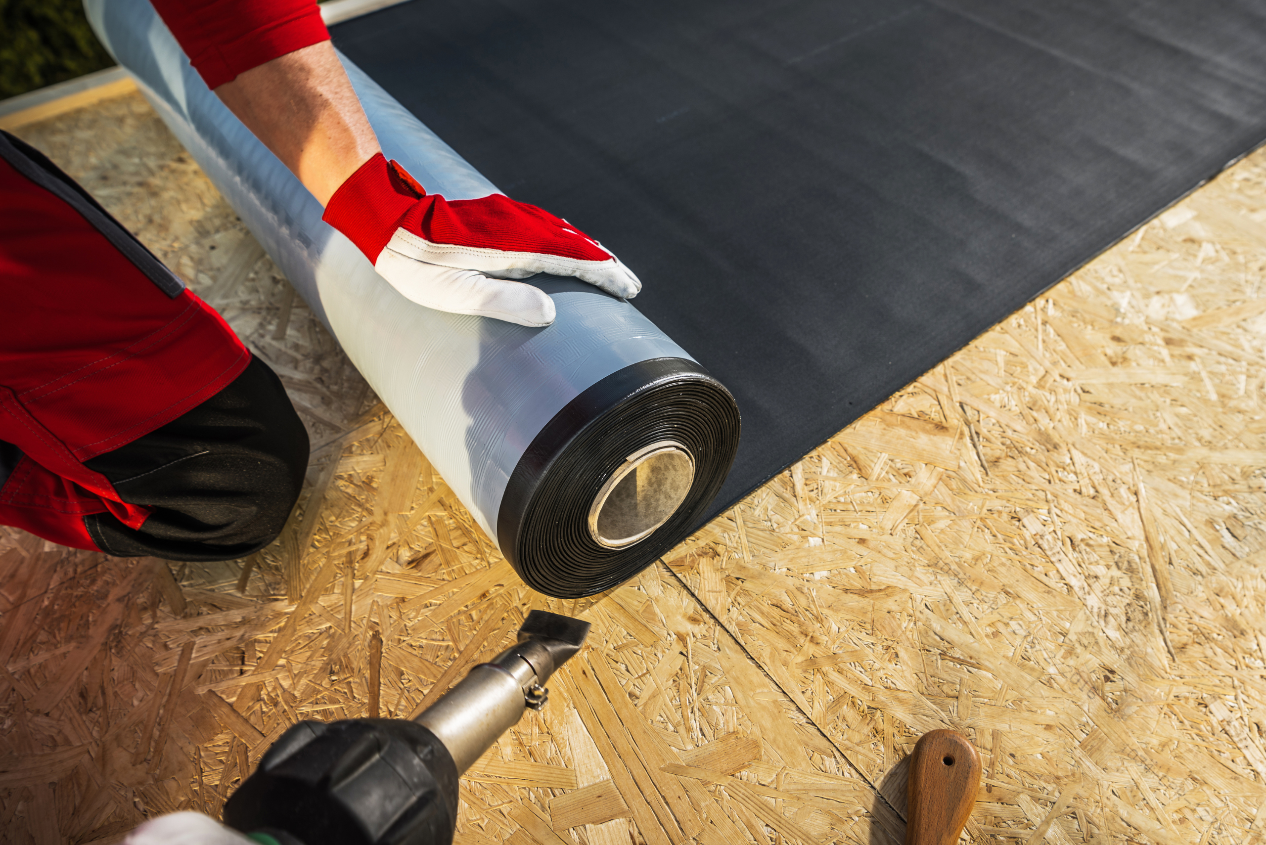 Worker rolling weather resistant material on top of plywood.