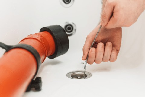 Red plunger and someone's hands using a drain snake.