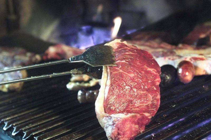 Metal tongues holding a steak on top of a grill.