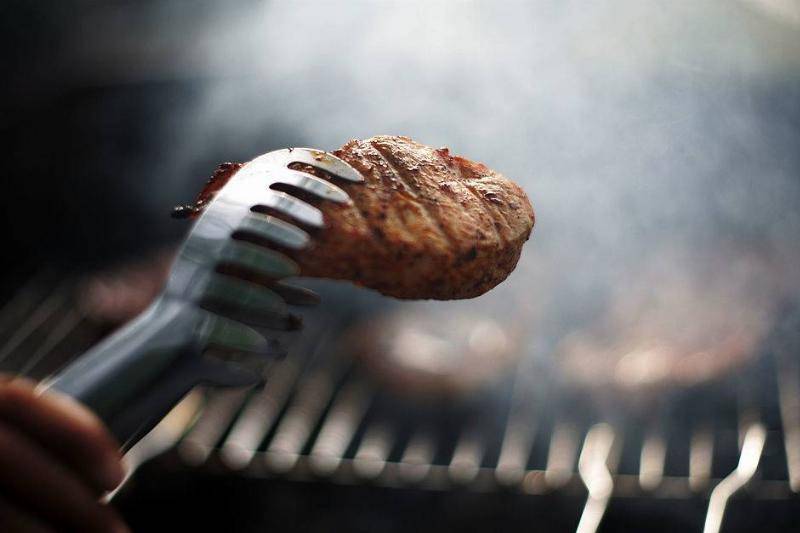 Metal tongues holding meat flanked by smokey BBQ.