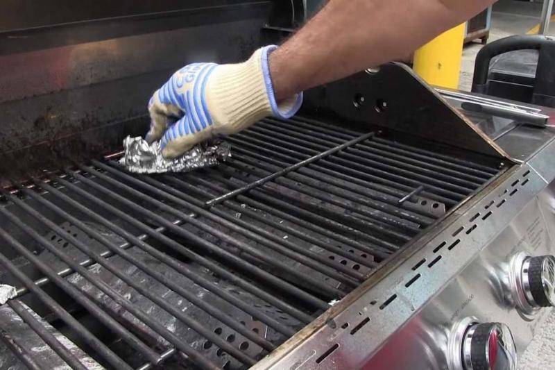 Person wearing gloves and using tin foil ball to clean BBQ.