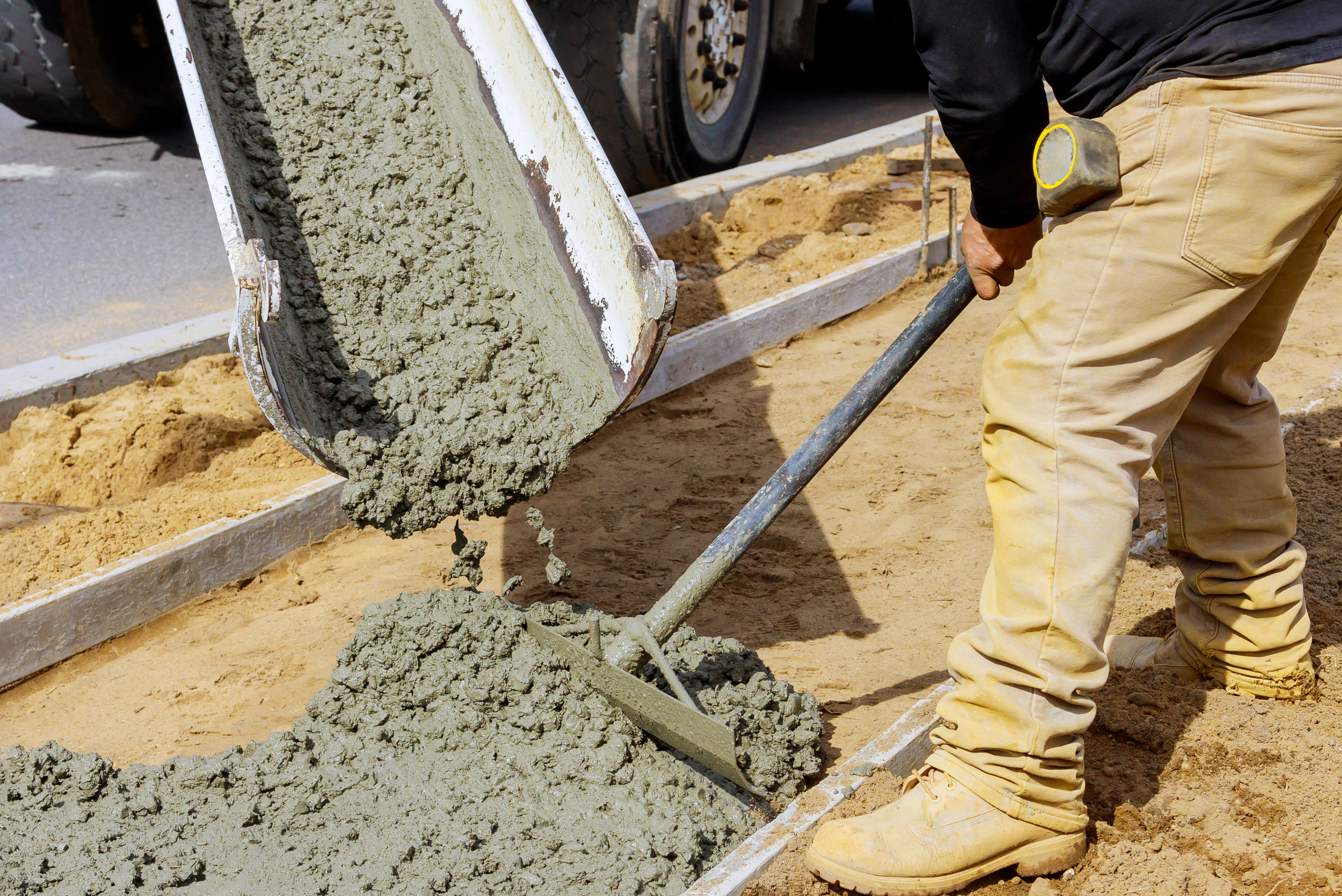 Pouring concrete mix from truck and worker spreading it out.