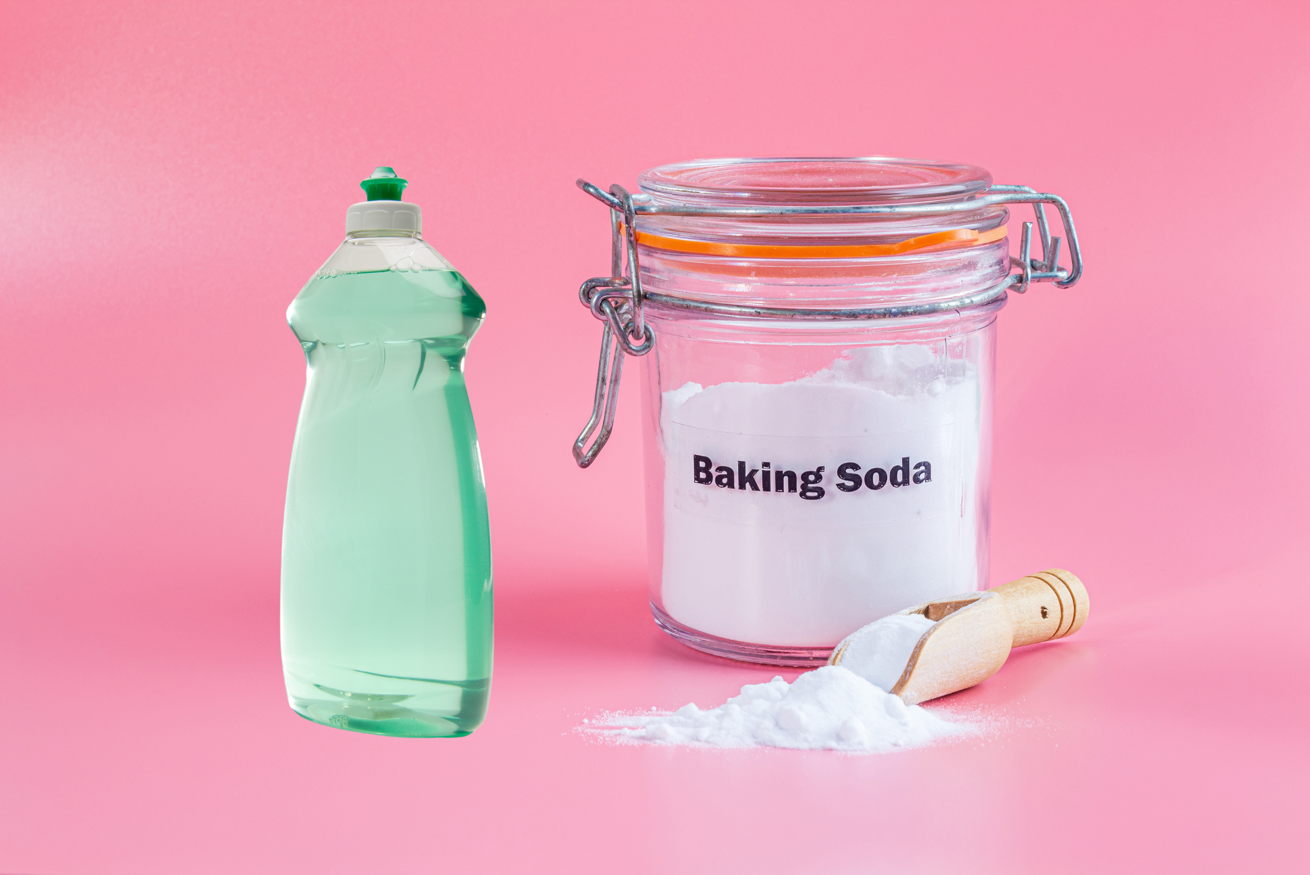 A jar labelled baking soda and a bottle of dish soap on pink background.