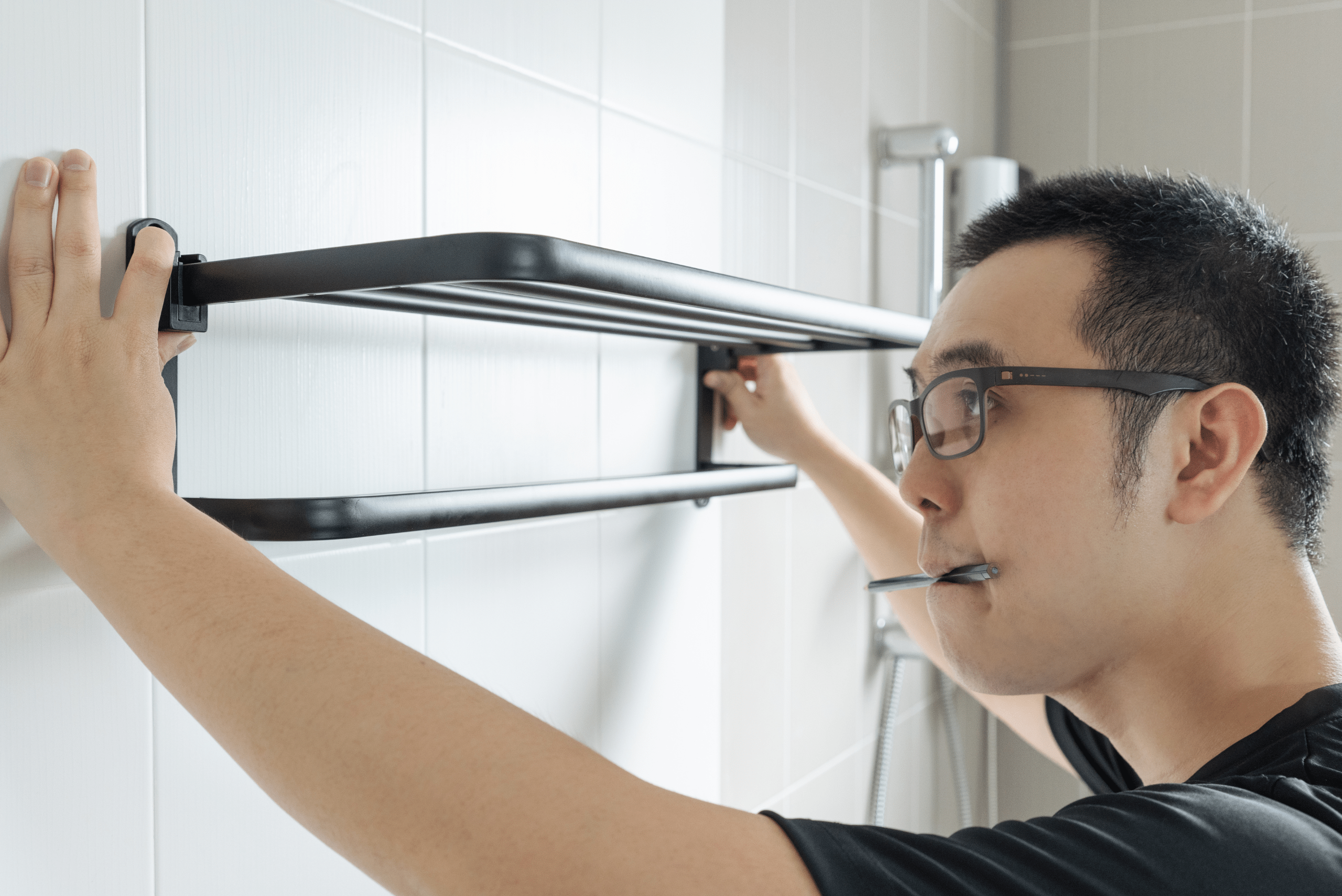 Man aligning towel holder on wall.