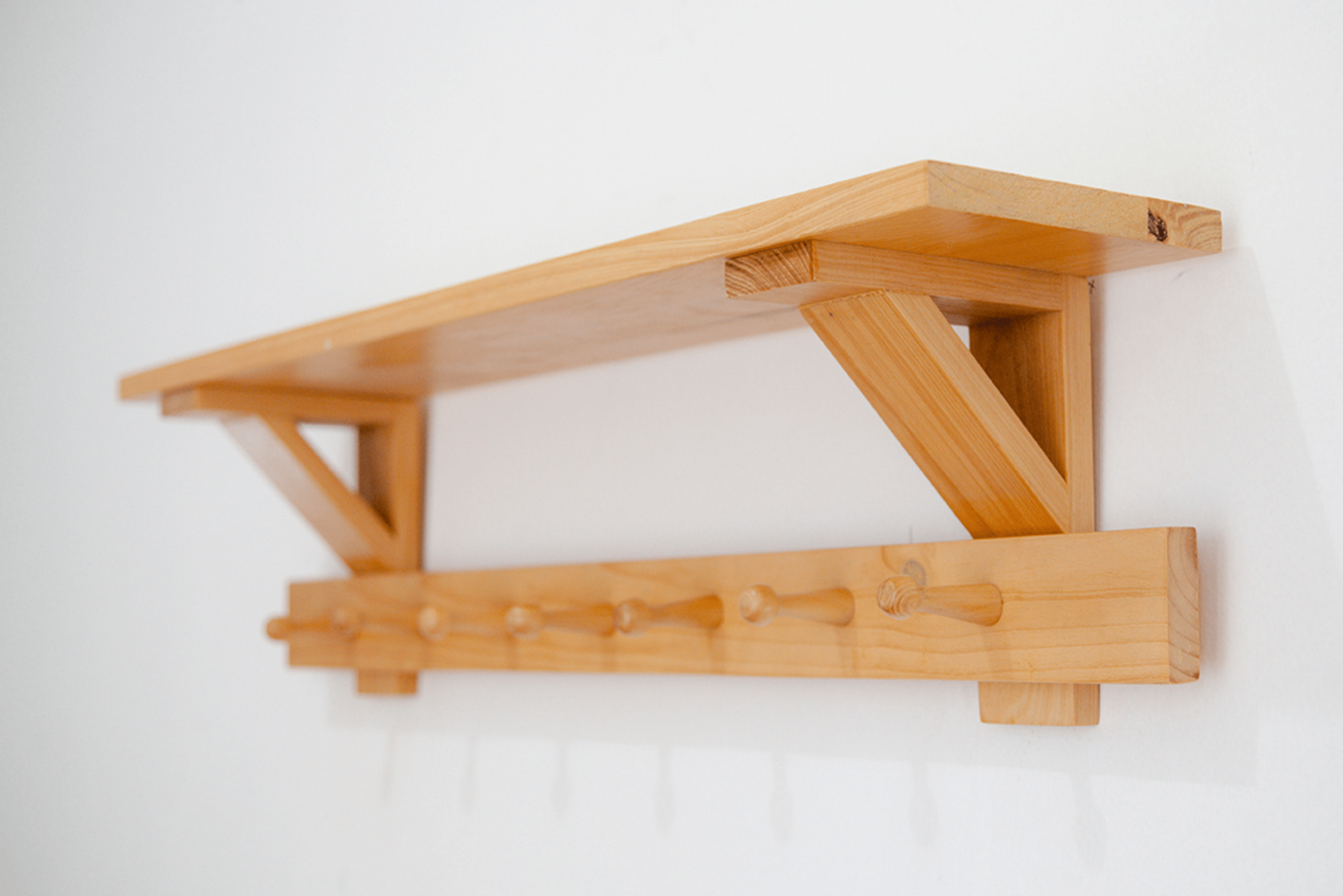 Floating wooden shelf with coat hangers underneath.