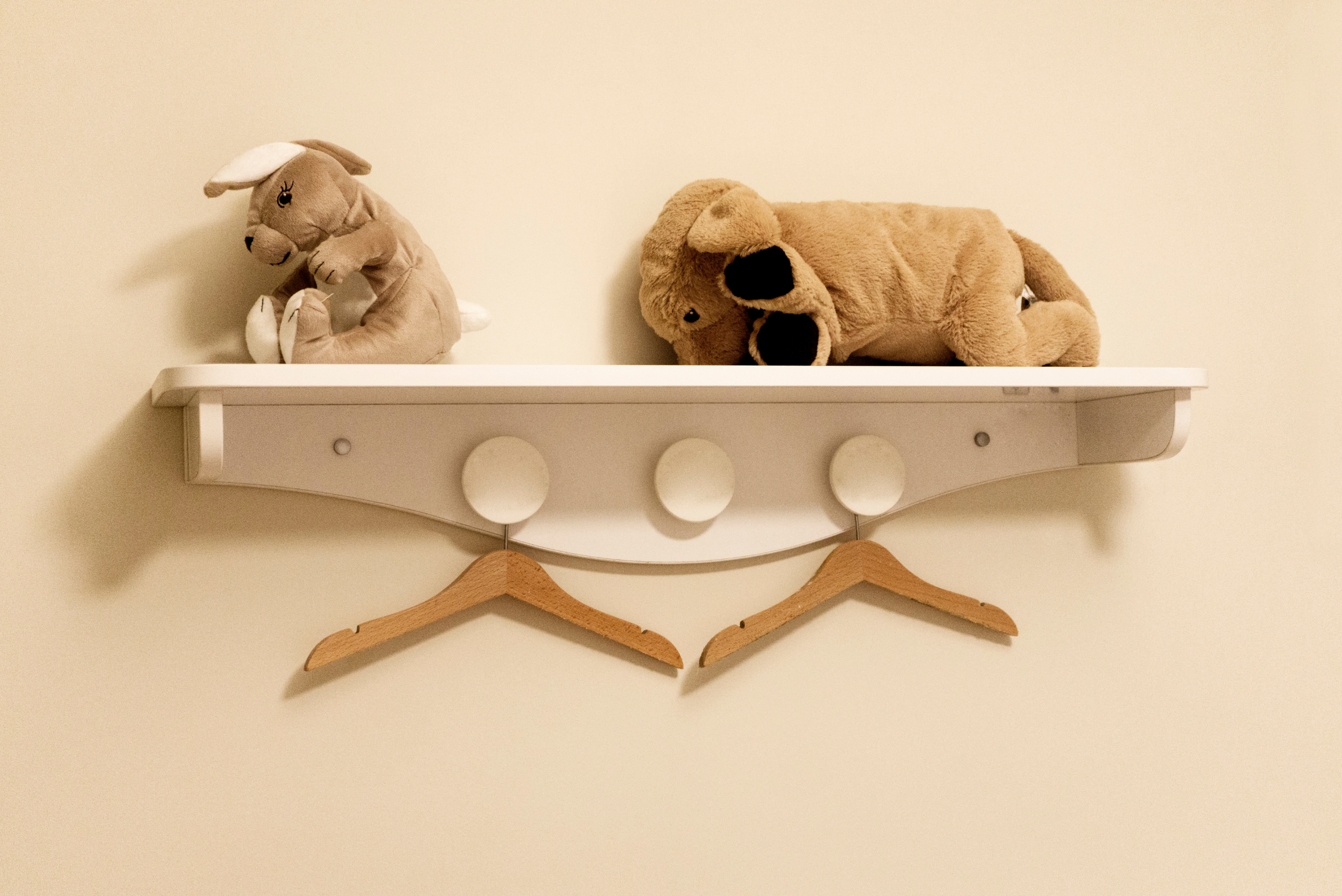 White wooden shelf with hangers and stuff toys on top.