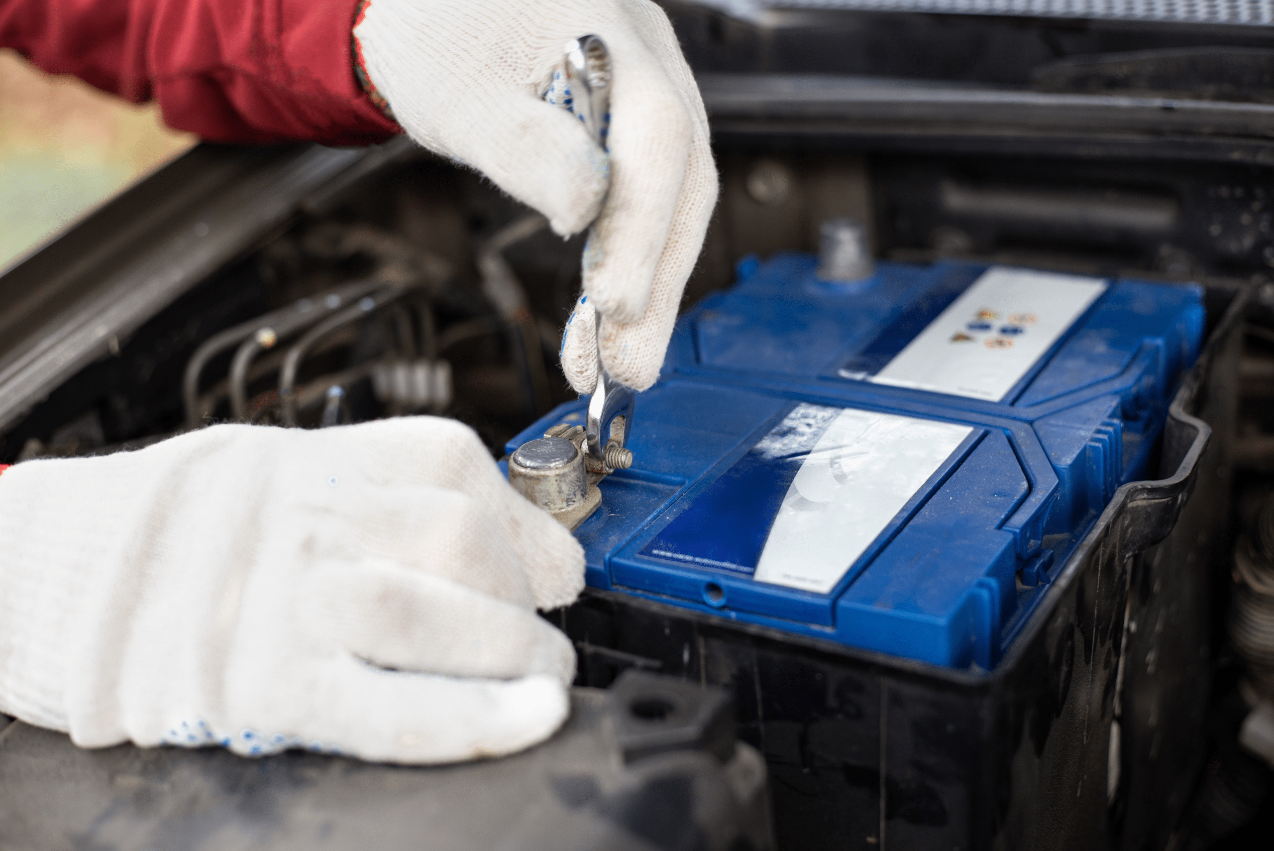 Someone's hands wearing gloves to undo battery terminal nuts with wrench.