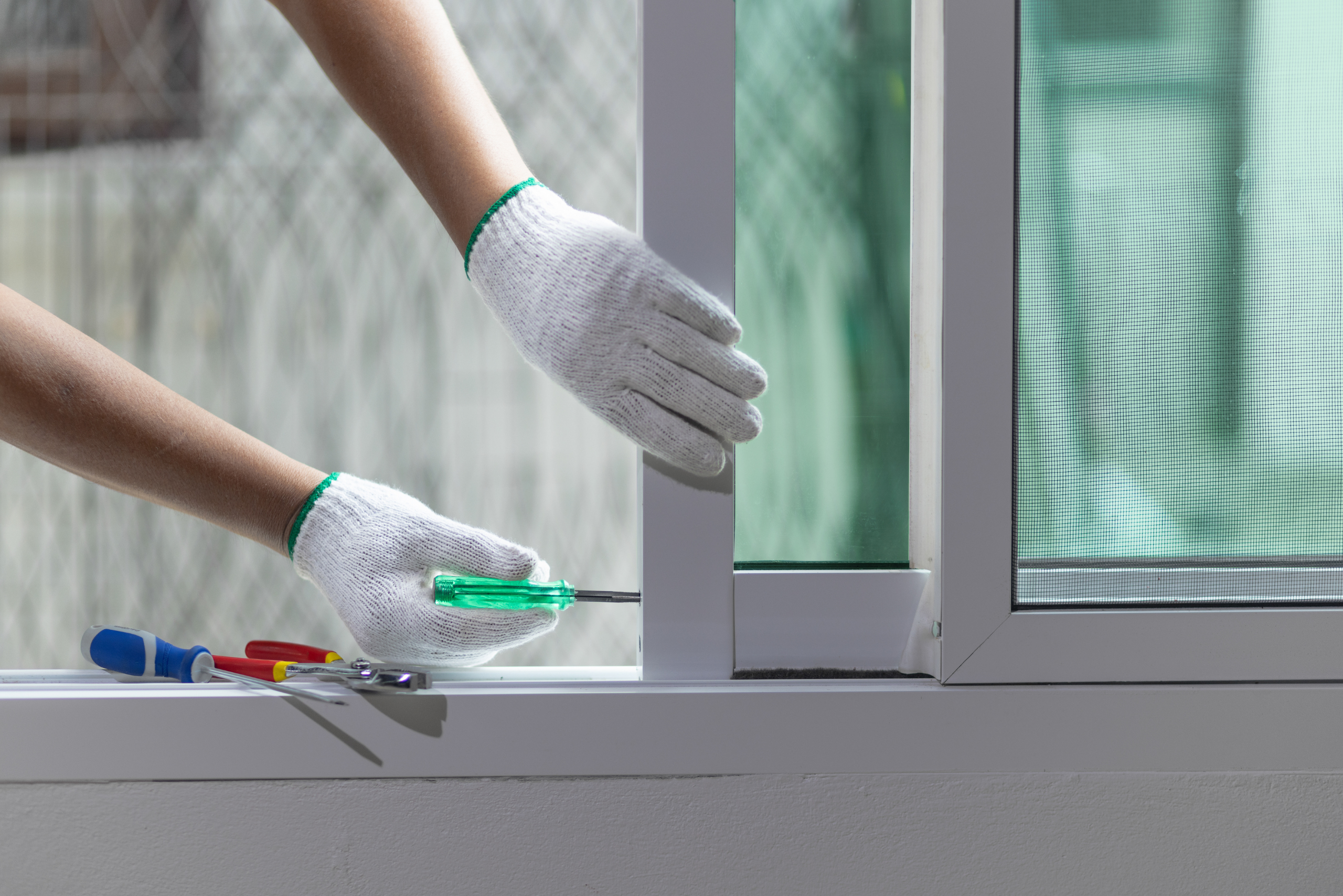 Person wearing gloves using a screwdriver to adjust window.