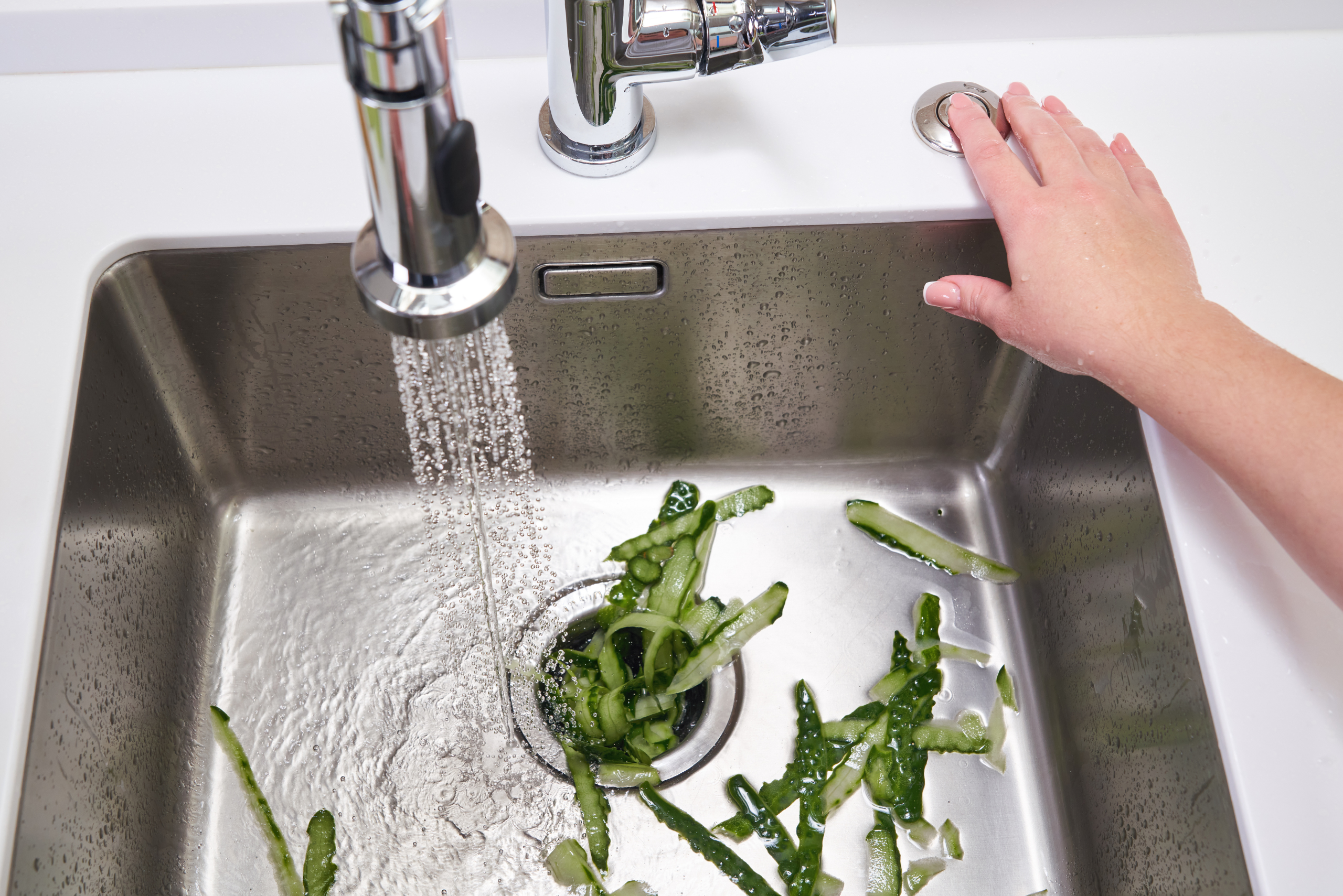 Putting water and cucumber peels through sink garbage disposal.