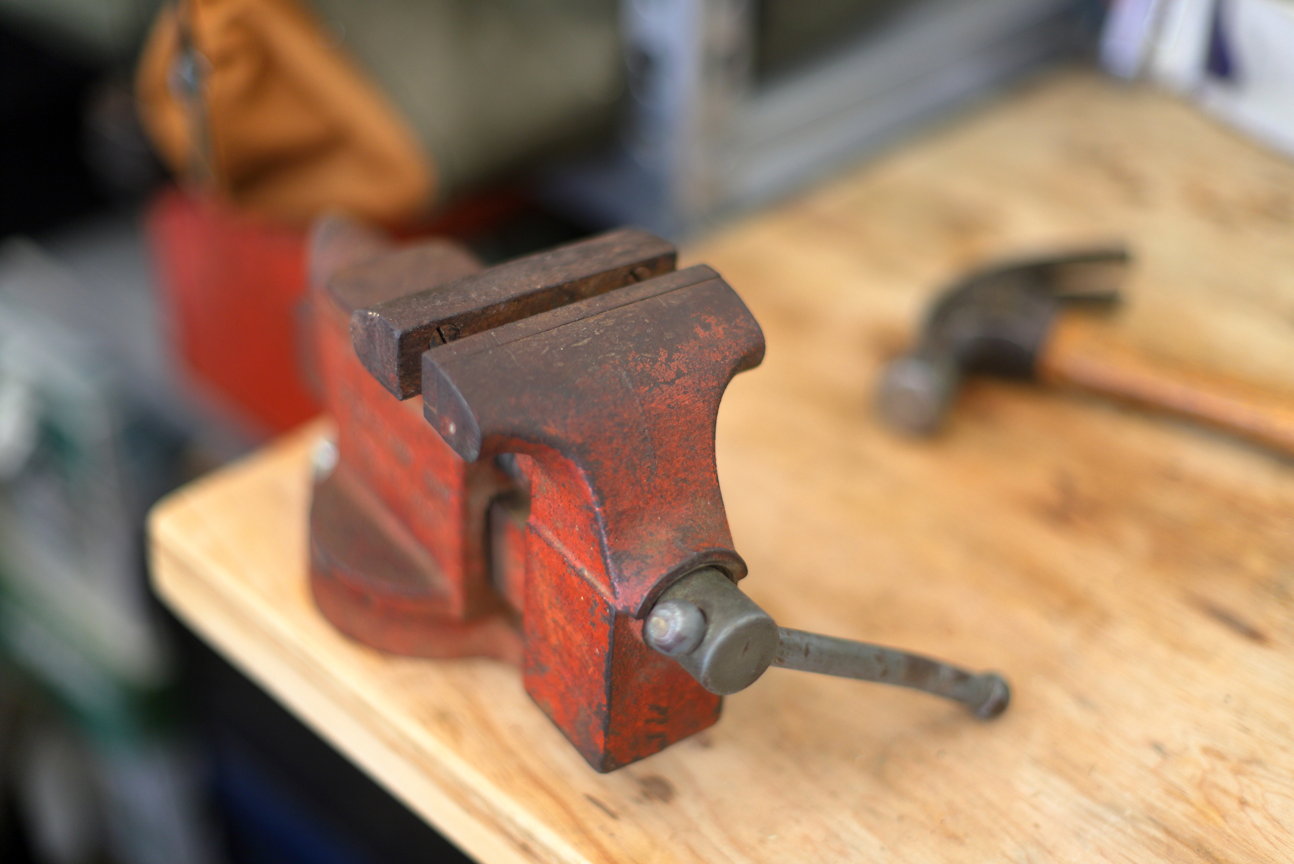 Worn red bench vise on table.