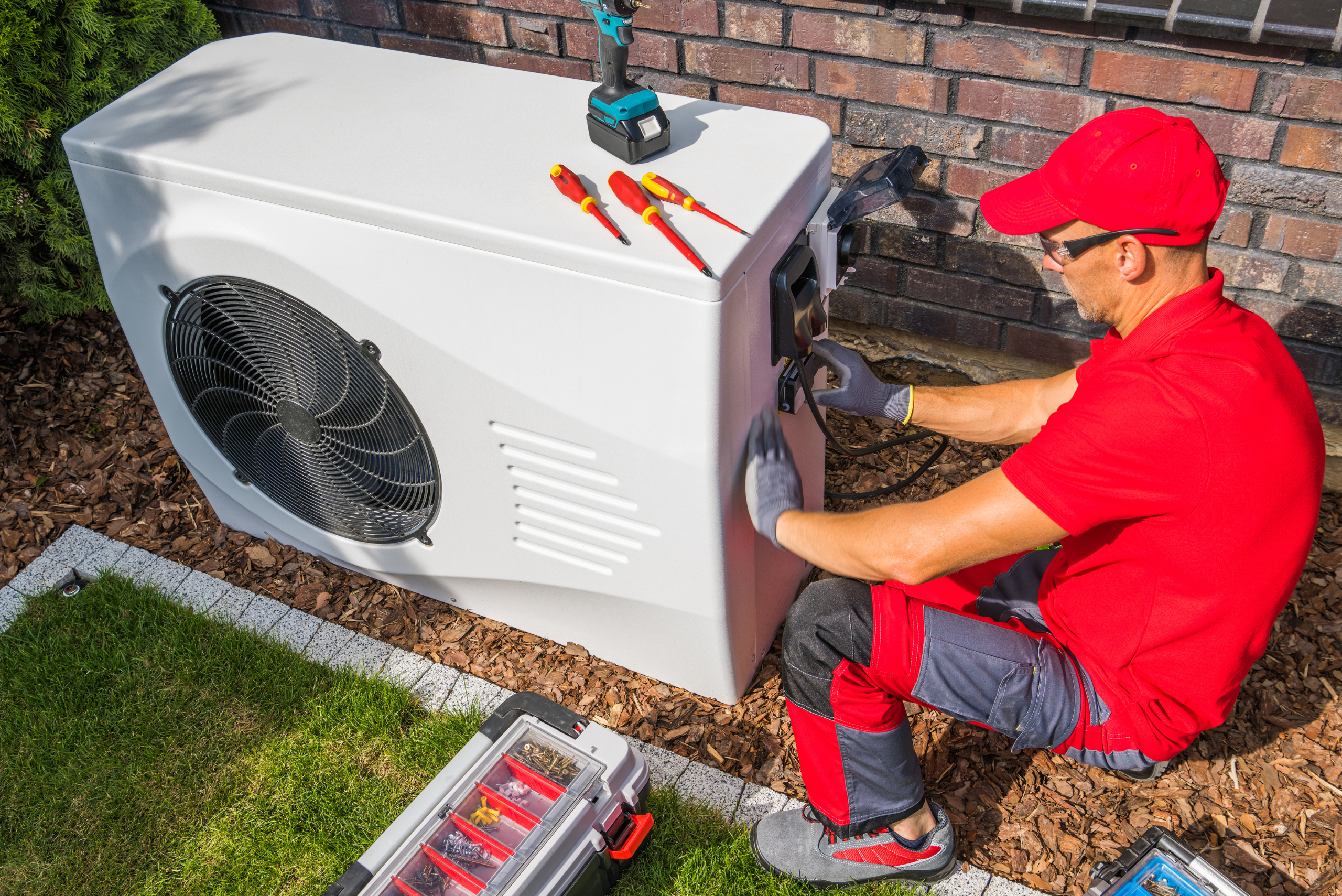 Worker wearing red servicing HVAC outdoor unit.