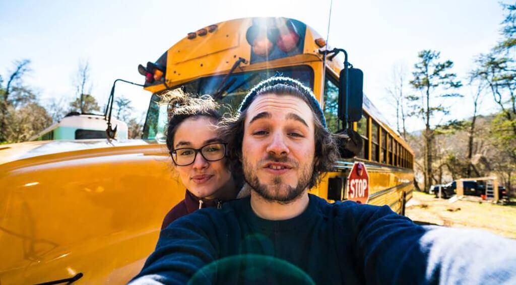 Couple posing in front of a yellow bus.