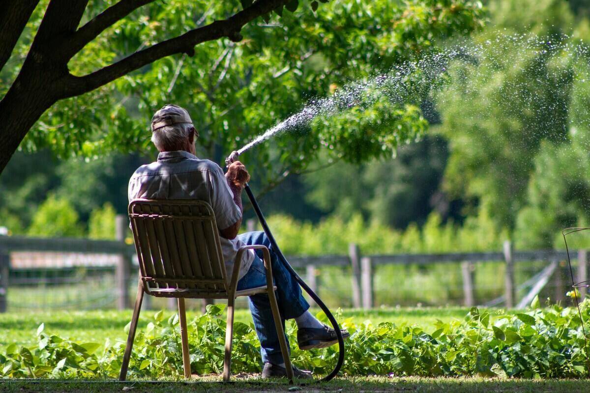 Man sitting on a chair watering the grass.