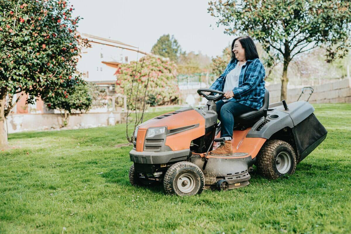 Woman using an orange sitdown lawn mower.