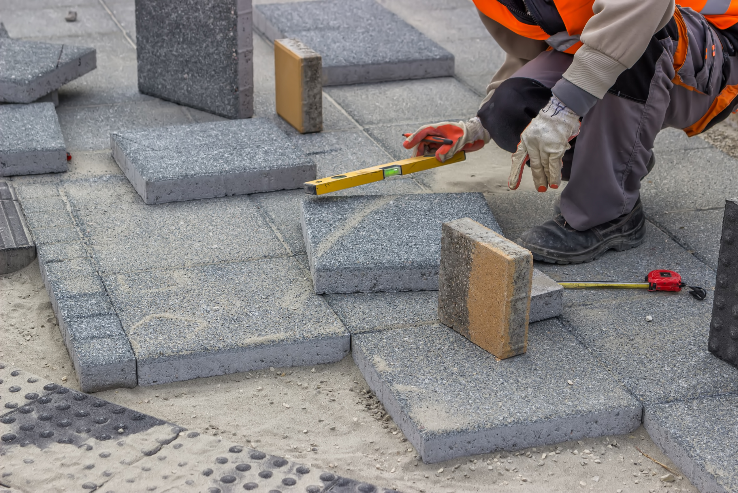 Man with level working on installing concrete pavers.