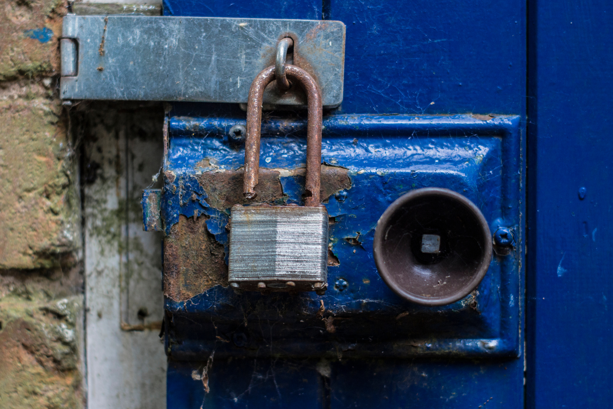 A rusty padlock that's open on a blue metal door.