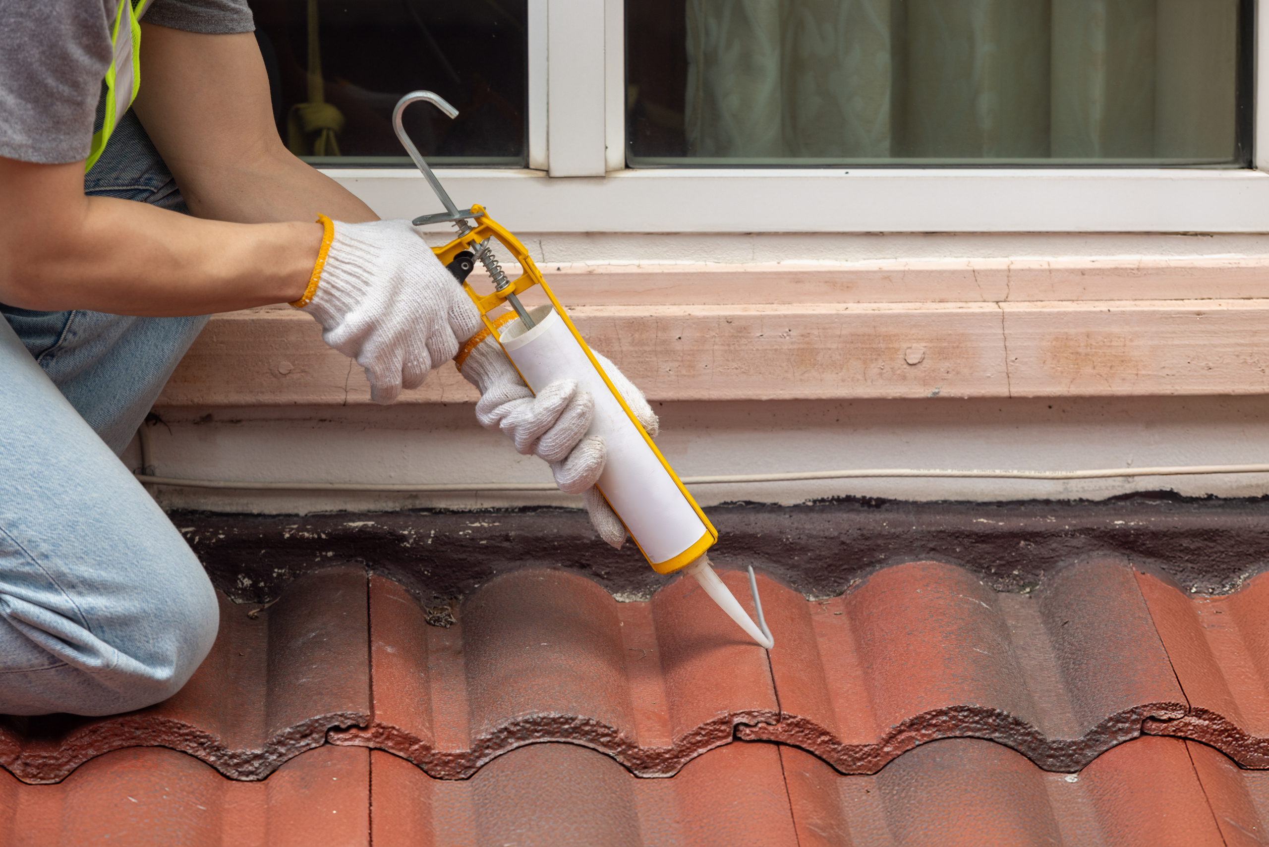 Worker applying caulking to red roof.